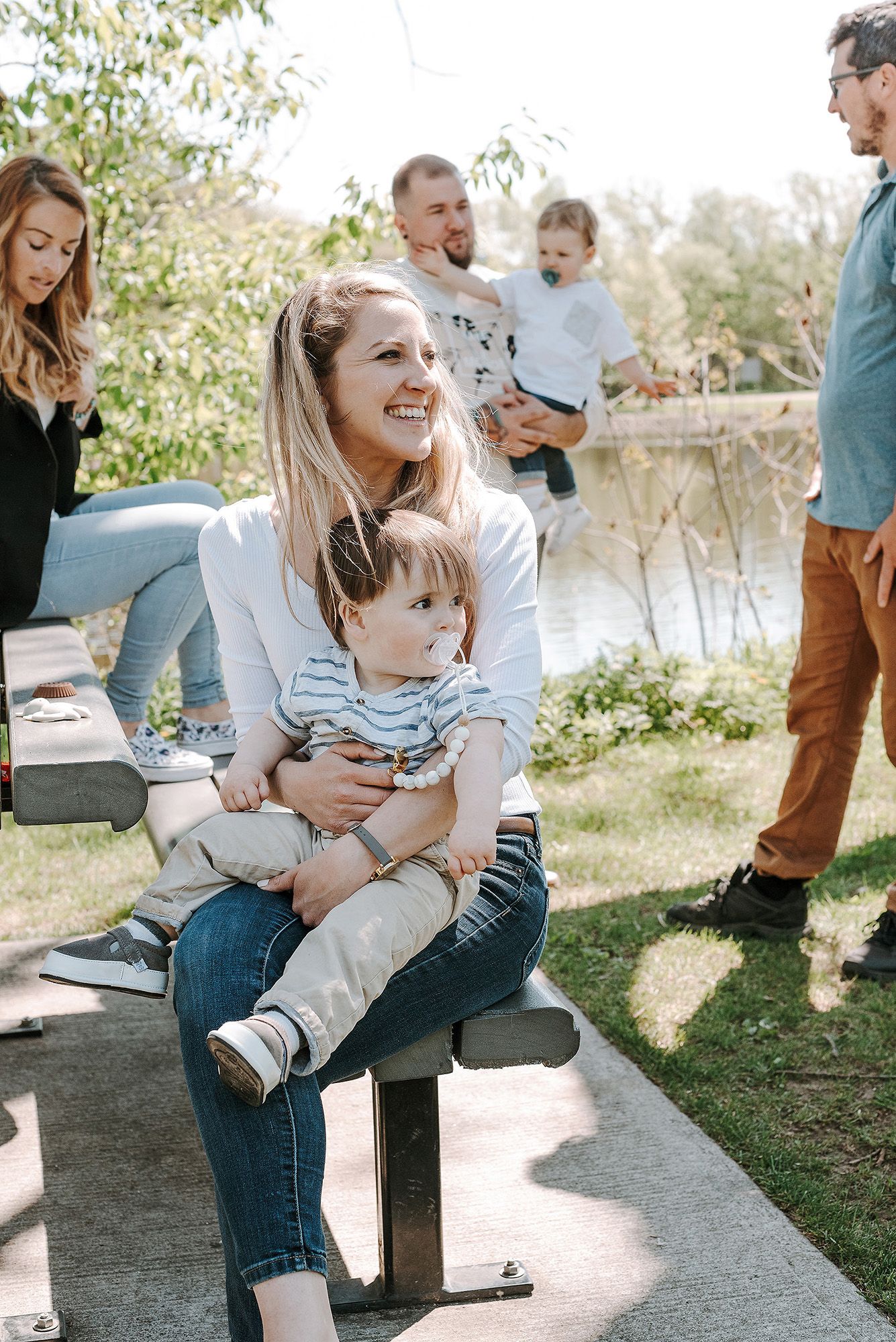 A sweet outdoor family moment captured on a wooden bench by a lake in natural sunlight.