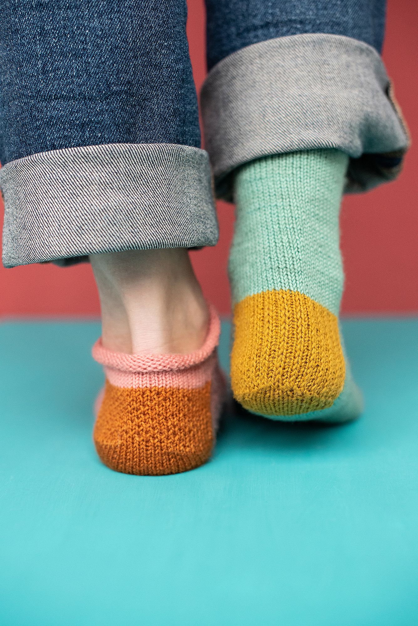 Close-up of mint green knitted socks with mustard yellow heels against turquoise background.