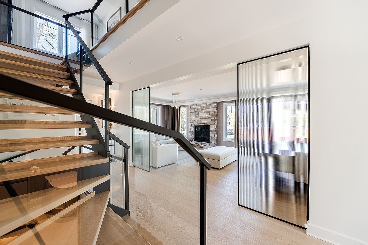 Modern spiral staircase with glass panels and wooden treads in an open concept living space.