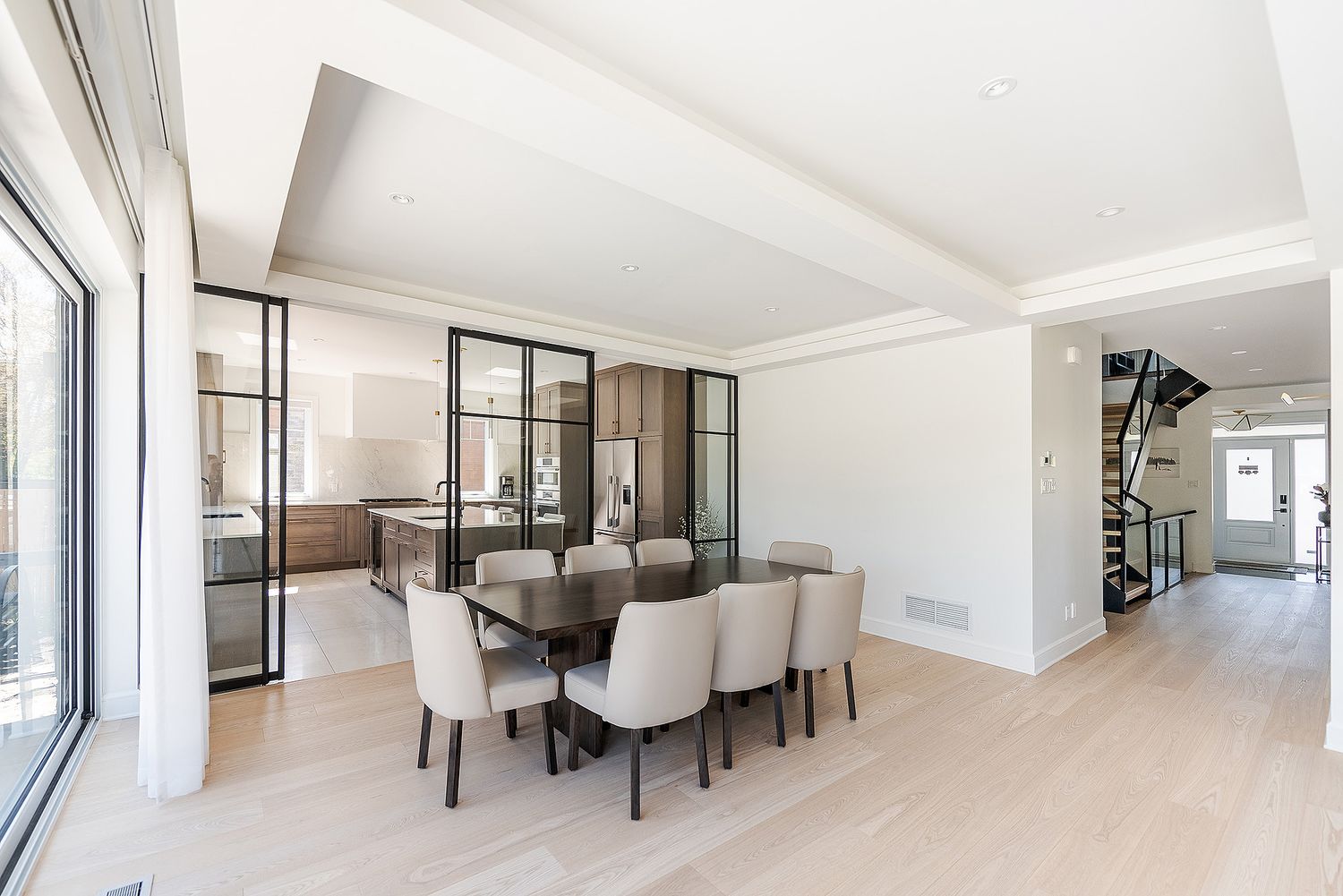 Modern dining room with light wood floors, glass partitions, and neutral upholstered chairs around a dark dining table.
