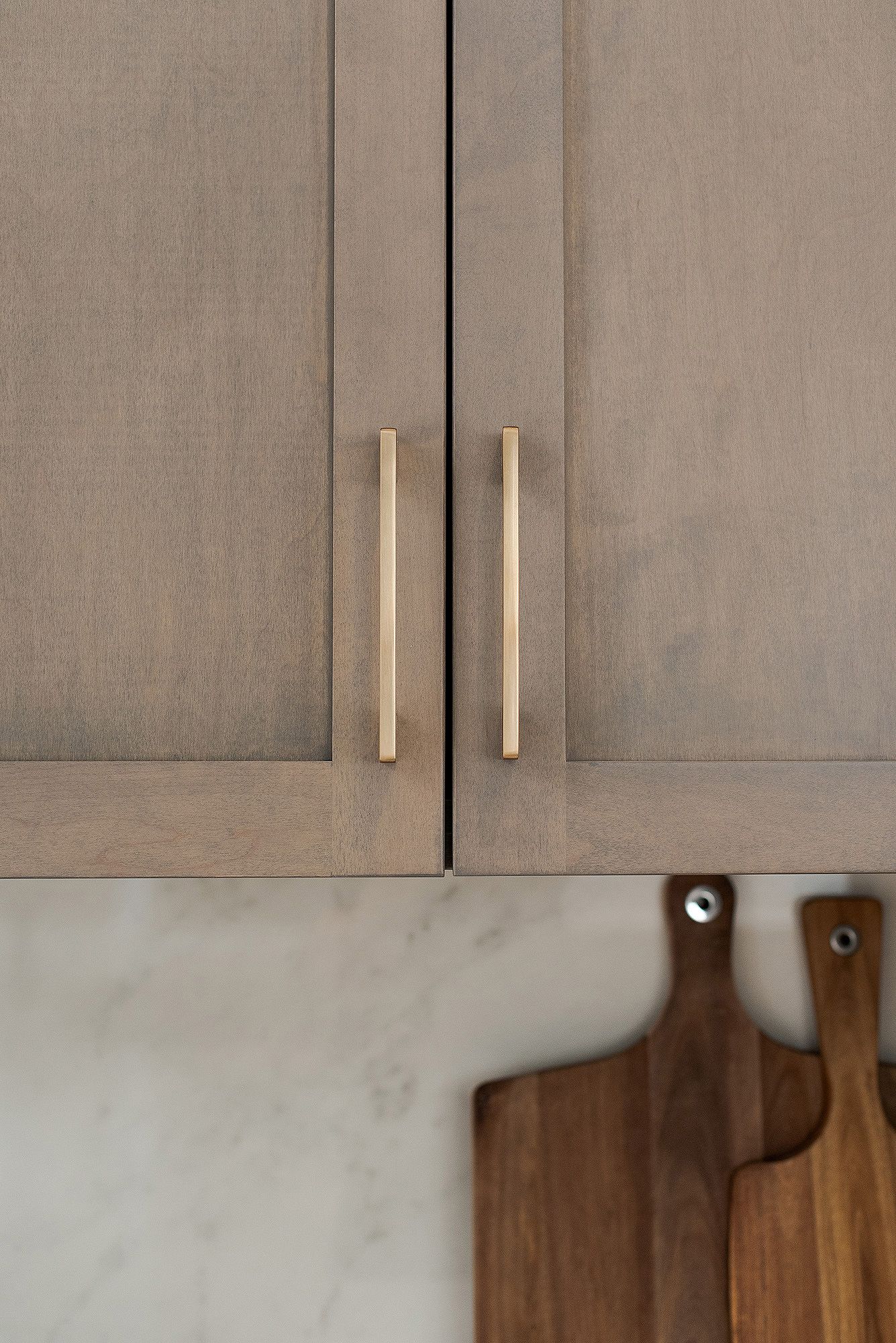 Close-up of taupe kitchen cabinet doors with sleek brass handles and textured finish.