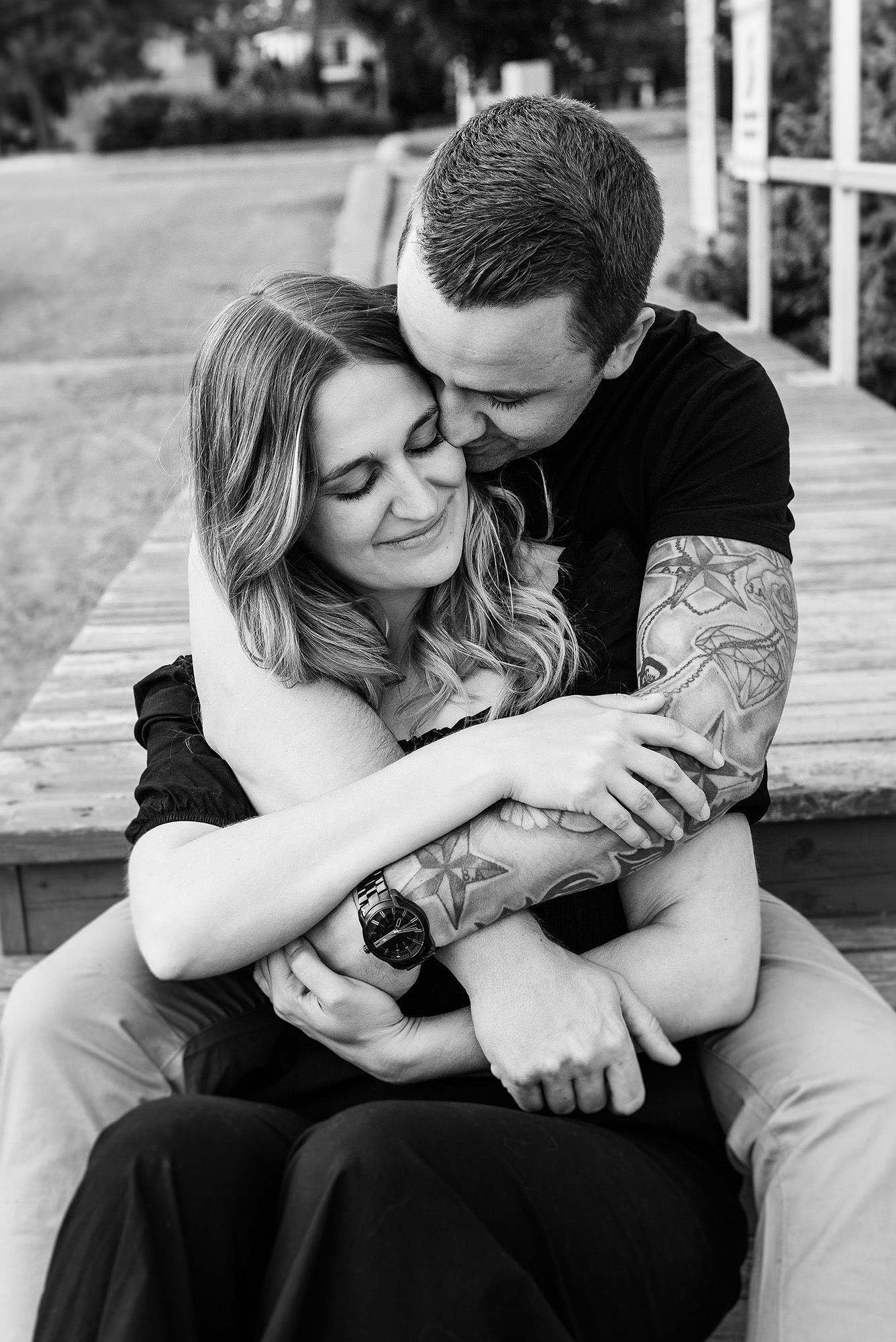 A tender black and white portrait of a couple embracing on a wooden deck.