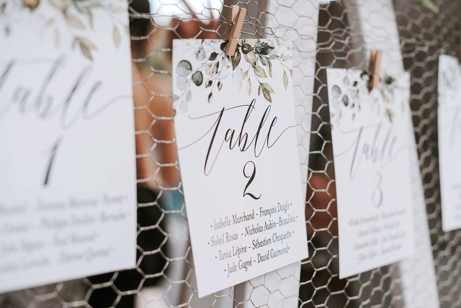 Wedding seating chart with table numbers displayed on white cards against a wire mesh backdrop.