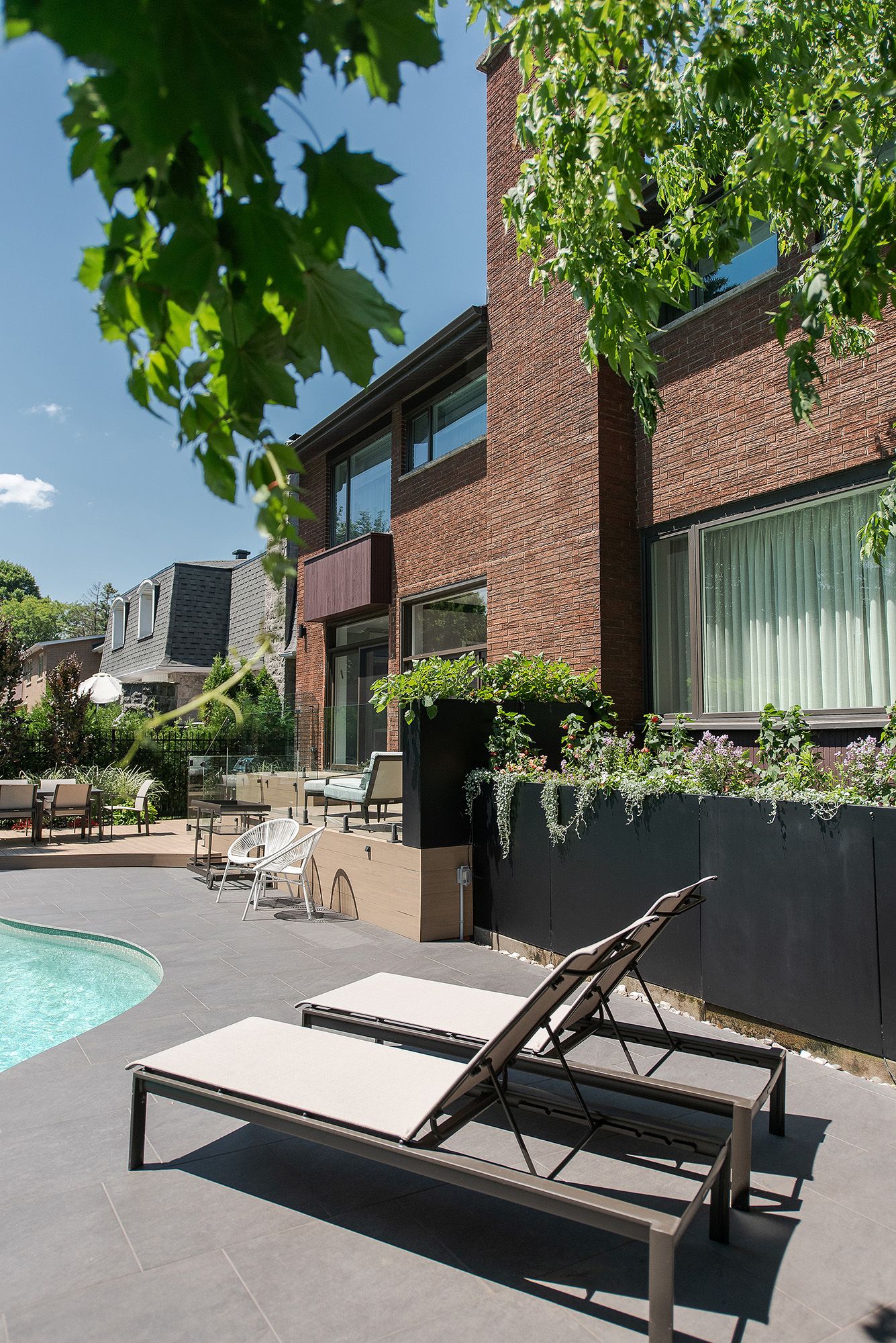 Modern outdoor pool area with sleek lounge chairs and brick building facade surrounded by lush green trees.