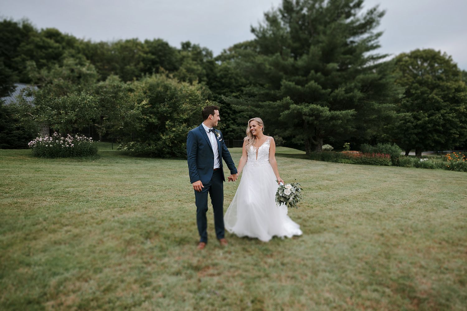 A couple walks together on a lush green hillside during an outdoor wedding celebration.