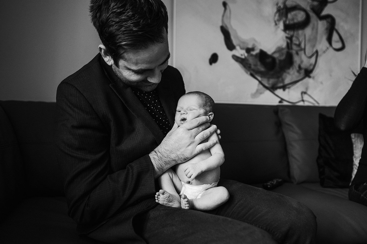 A tender black and white portrait of a parent cradling a newborn baby on a couch.