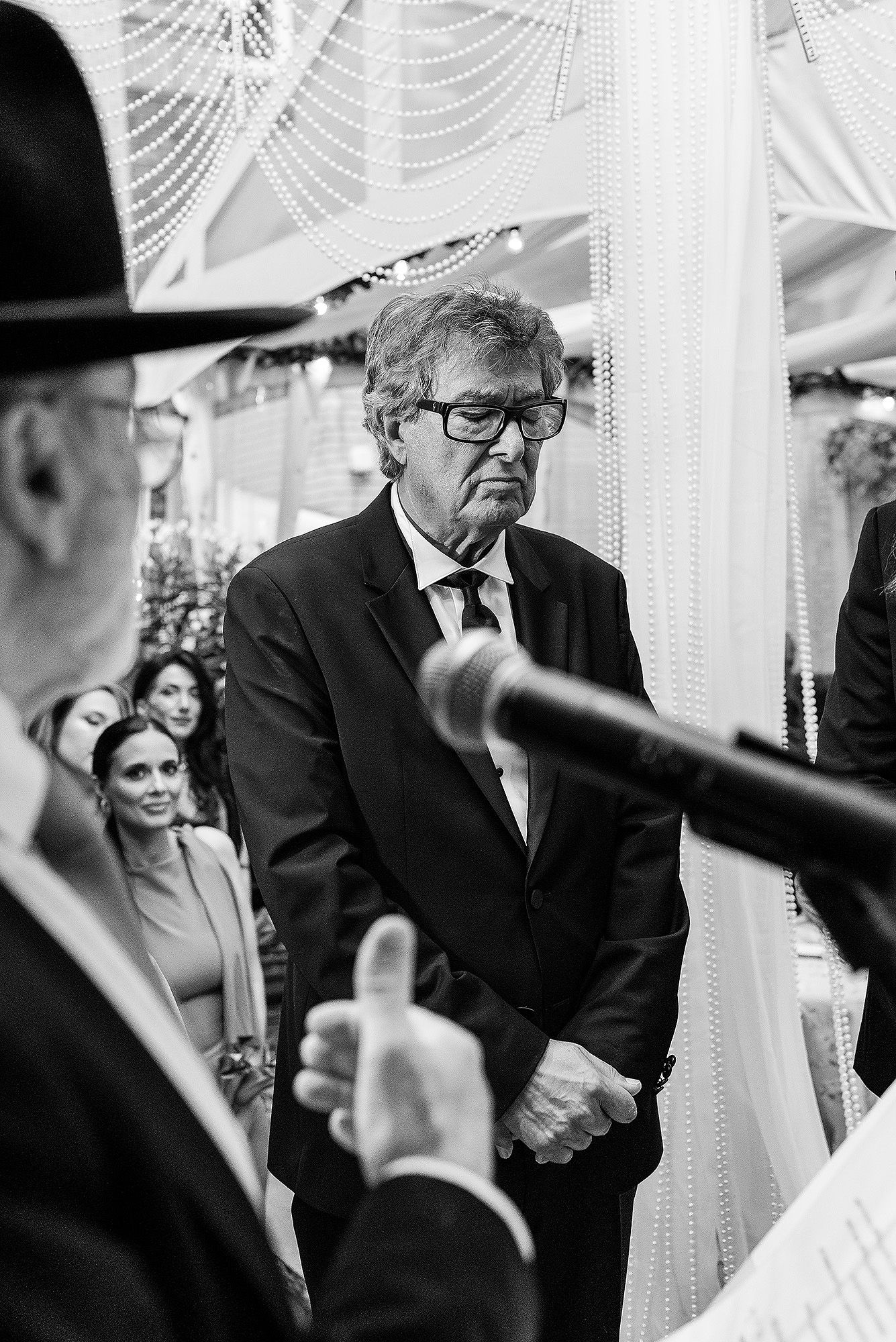Black and white photo of a wedding ceremony with guests and a canopy of white fabric decorations overhead.