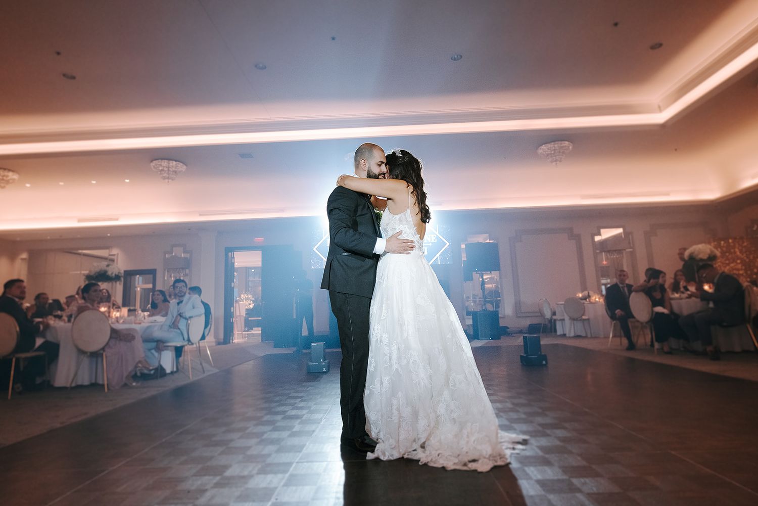 Bride and groom share their first dance in a dimly lit ballroom with fog effects on the dance floor.