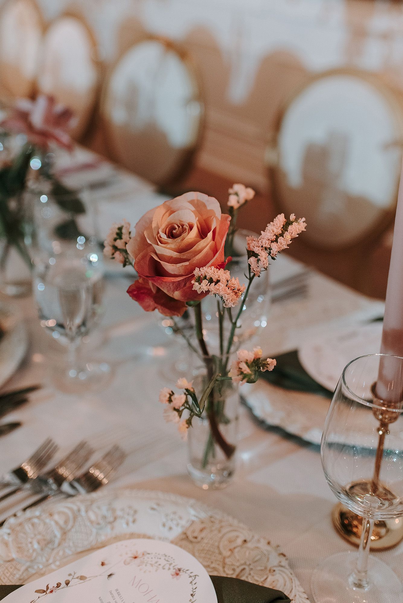 Romantic table decorations featuring peach roses in small vases with delicate lace details on white linens.