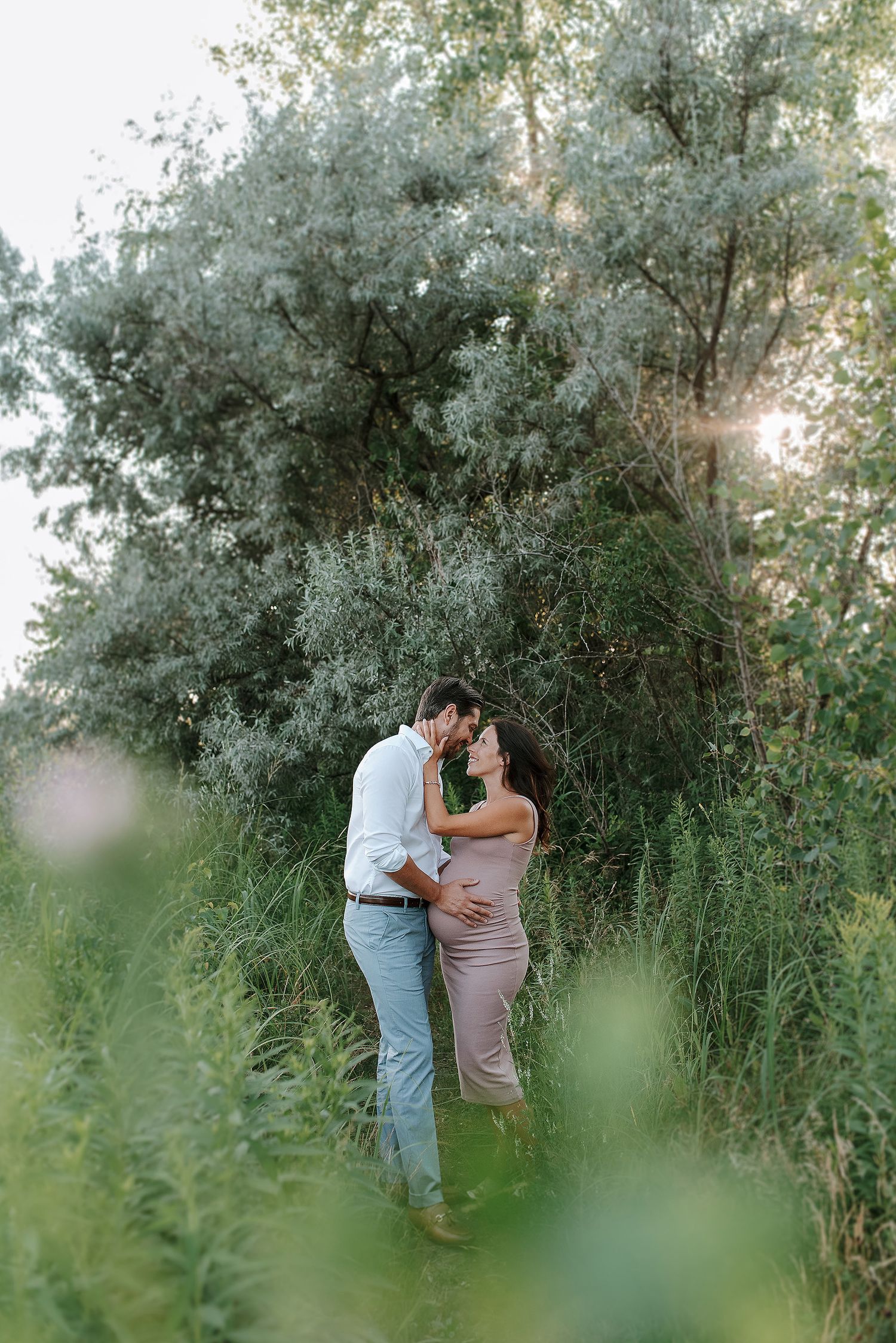 Romantic couple moment captured through foliage in a natural outdoor setting.