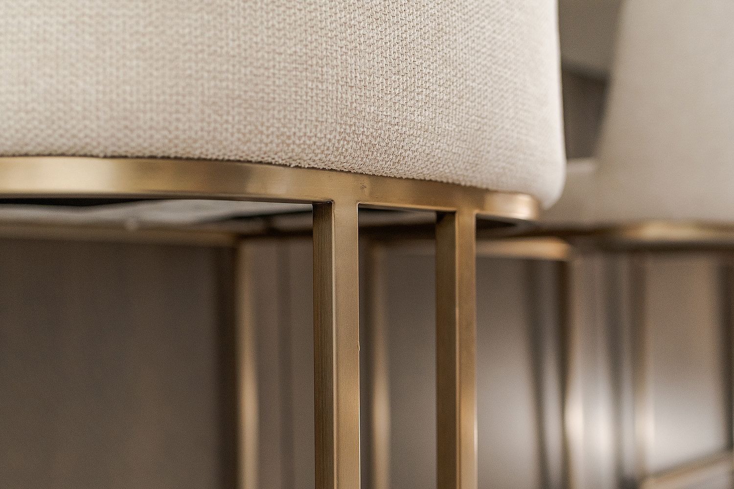 Close-up detail of a modern gold metal furniture base with beige upholstered cushion on top.