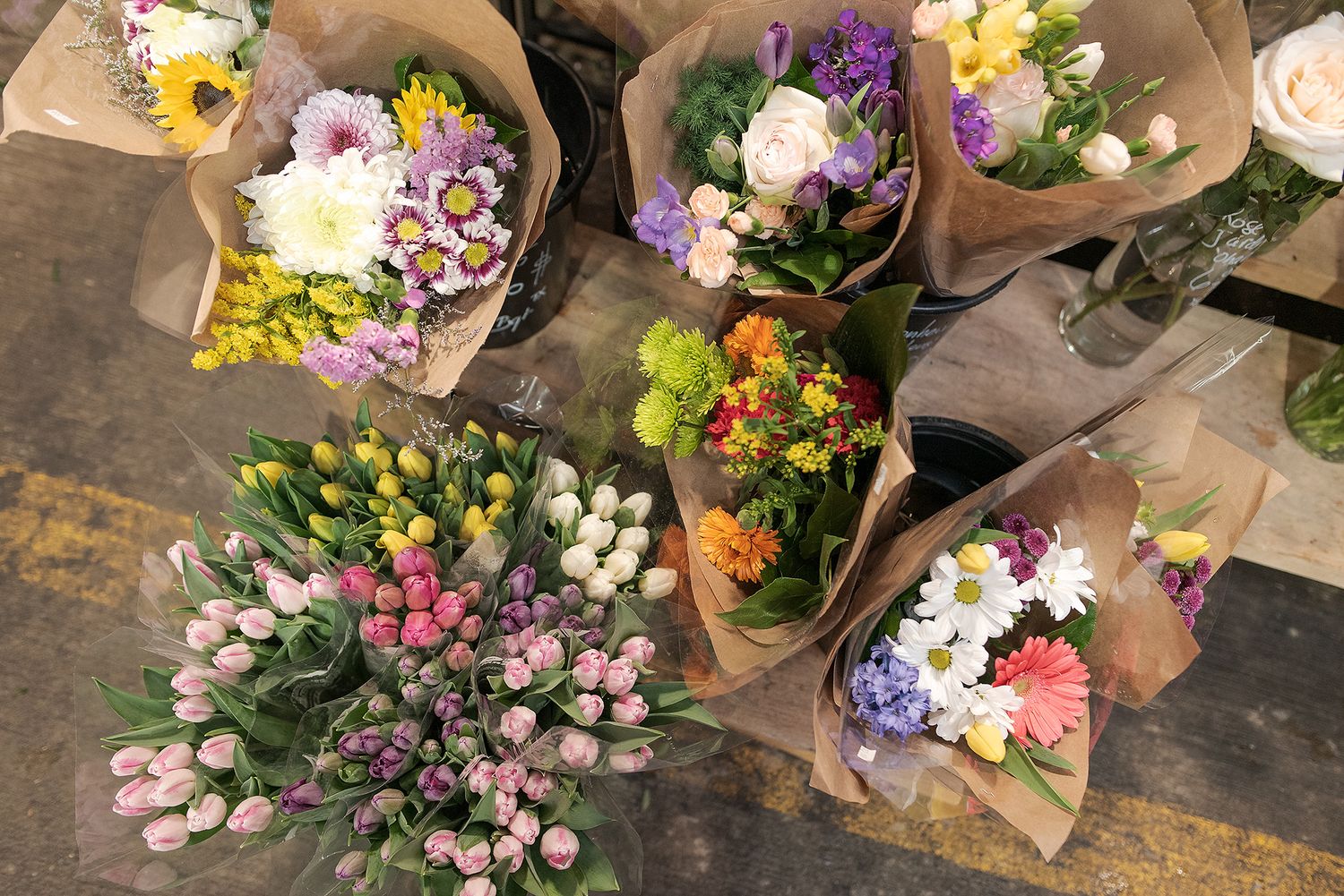 Overhead view of colorful flower bouquets wrapped in kraft paper displayed on a rustic wooden surface.
