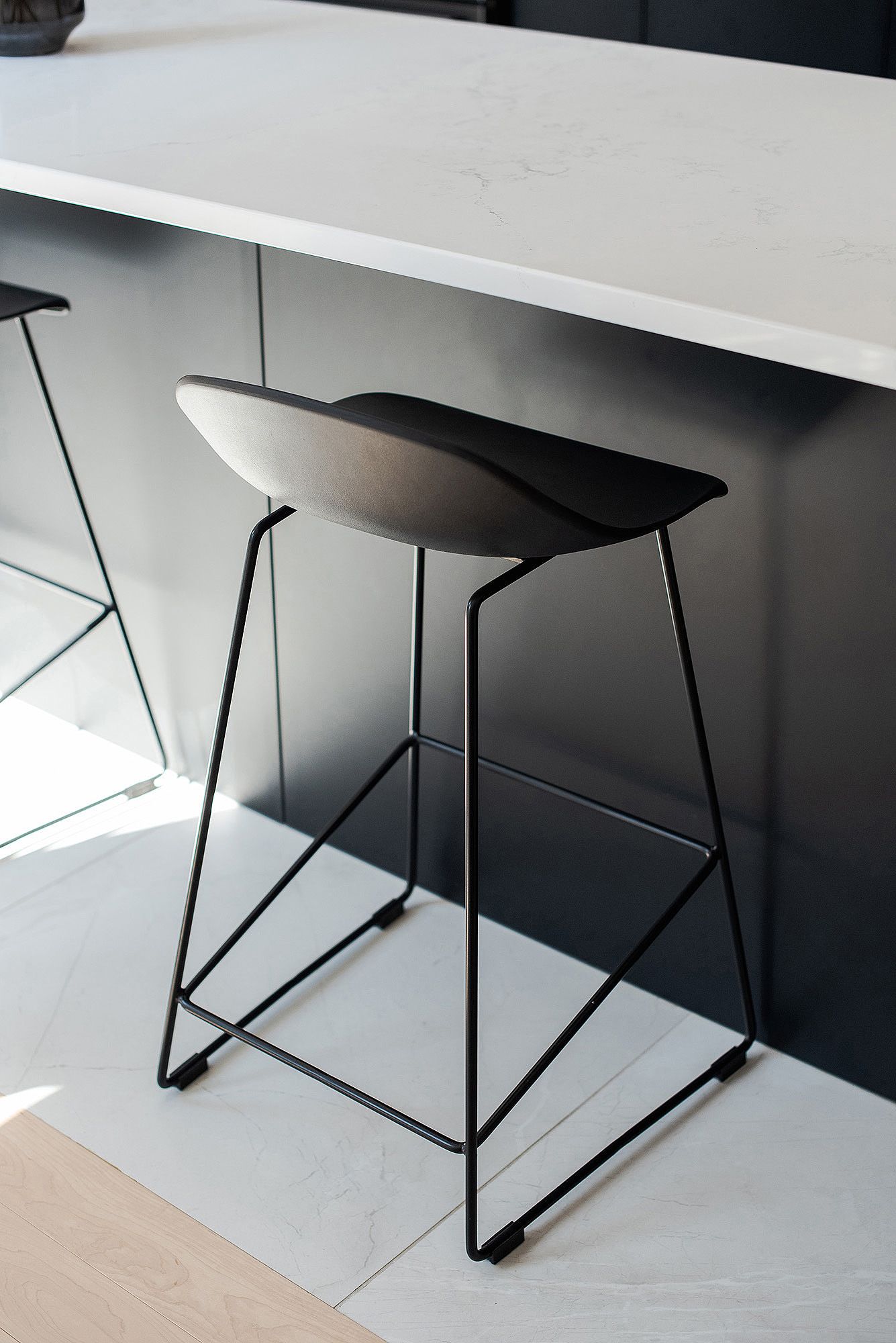 Close-up of modern black bar stools with geometric metal bases against white countertop.