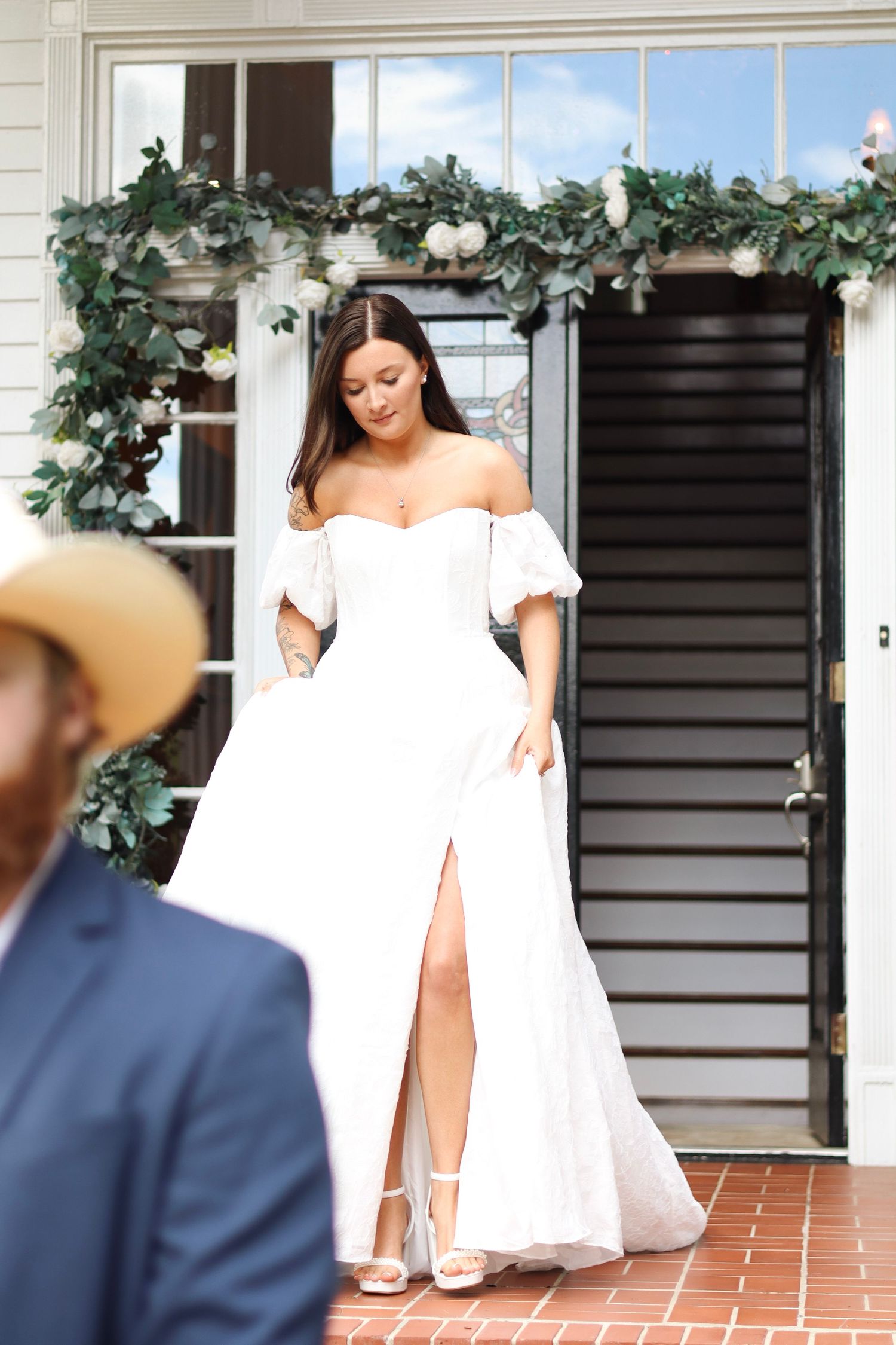 Wedding photos showing a bride in a white off-shoulder dress near a staircase with greenery decor.