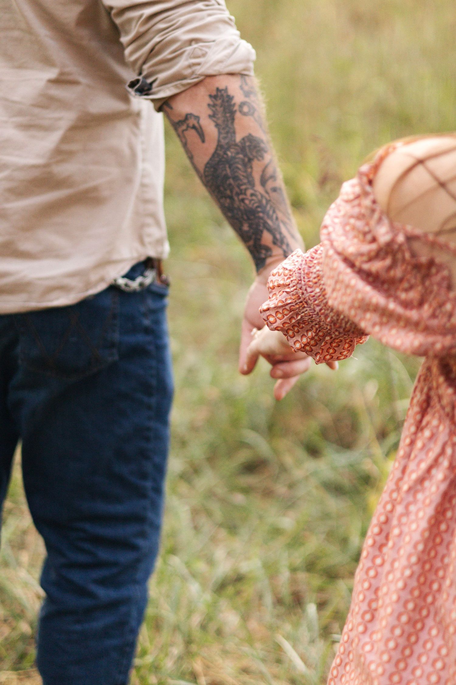 Tattooed hands reaching towards each other in a grassy field.