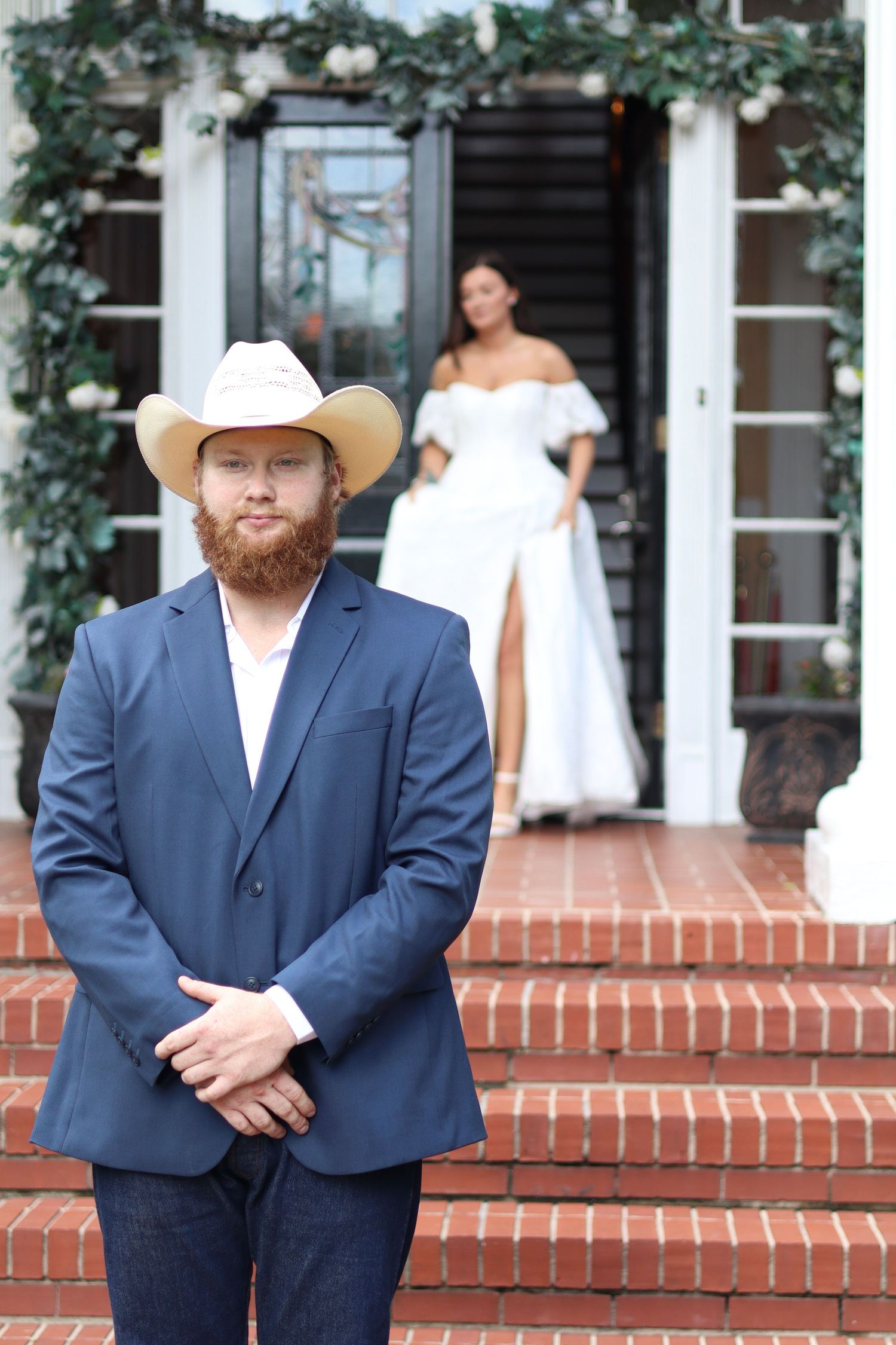 Wedding party members in navy suits and cowboy hats pose on brick steps near white columns.