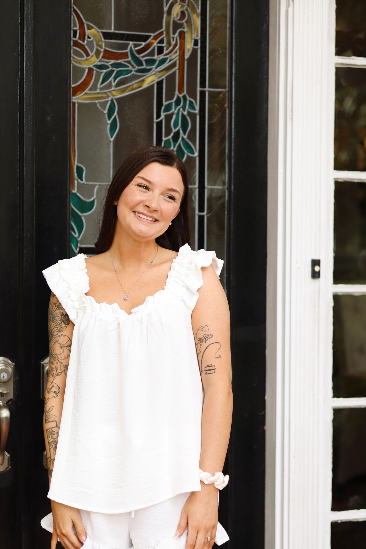 A white off-shoulder dress against decorative stained glass windows and dark doors.