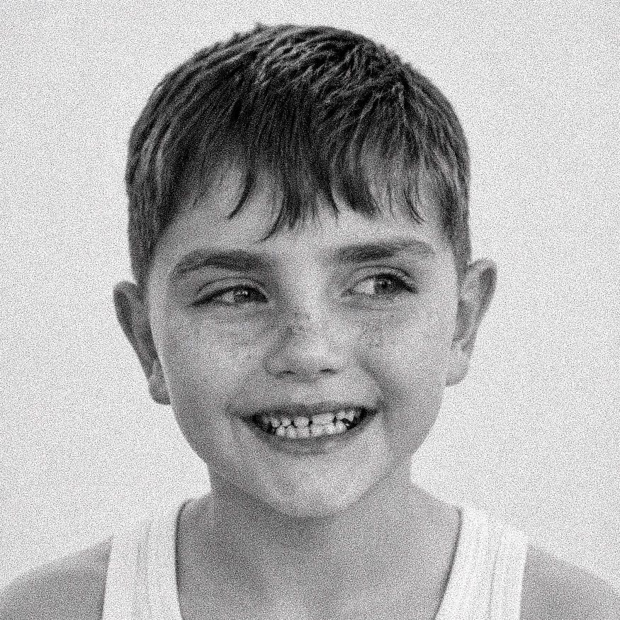 Black and white portrait of a smiling young boy with short hair and freckles wearing a white tank top.