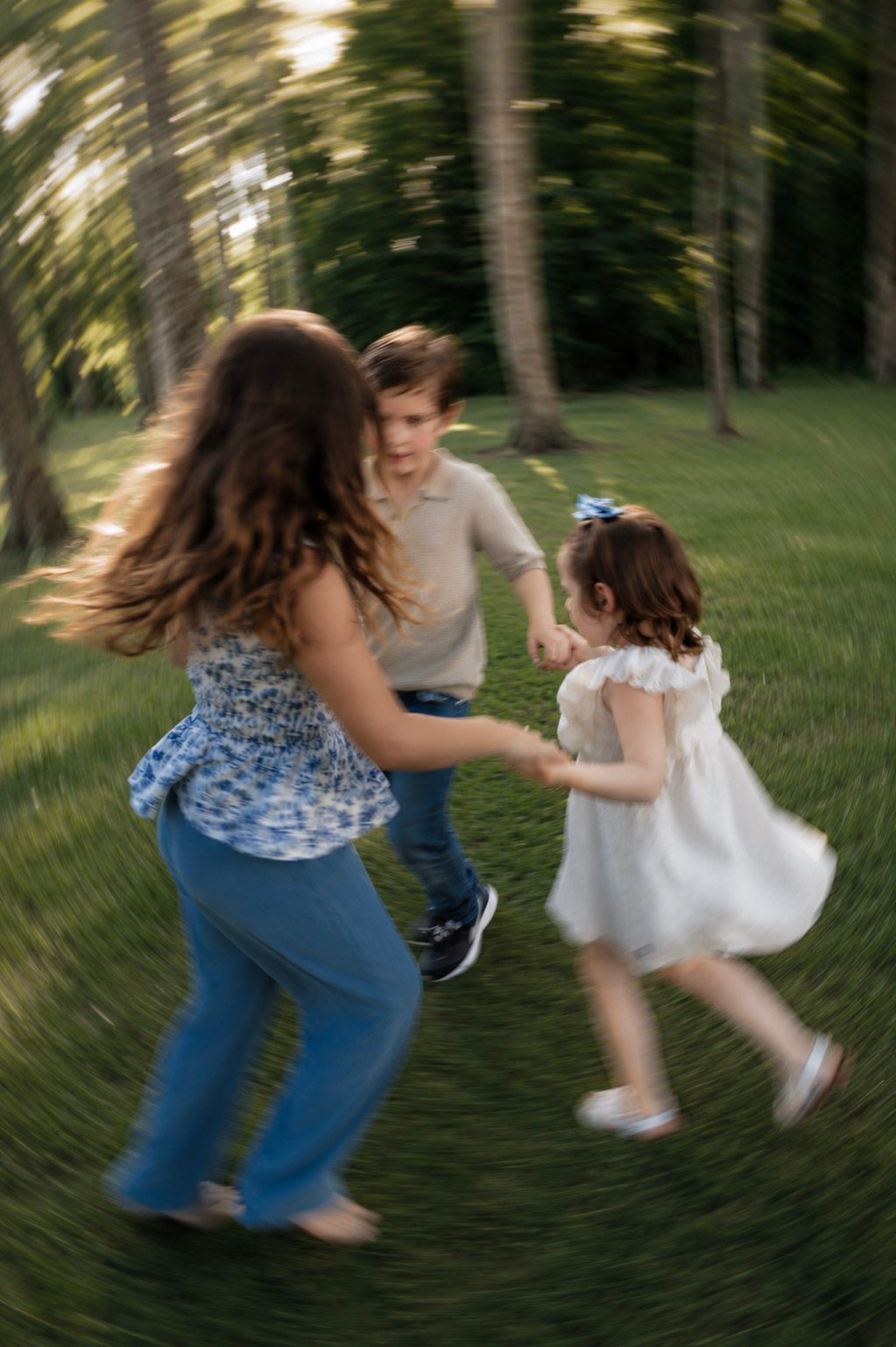 Three children joyfully spinning in a circle on green grass outdoors in a motion-blur photo.