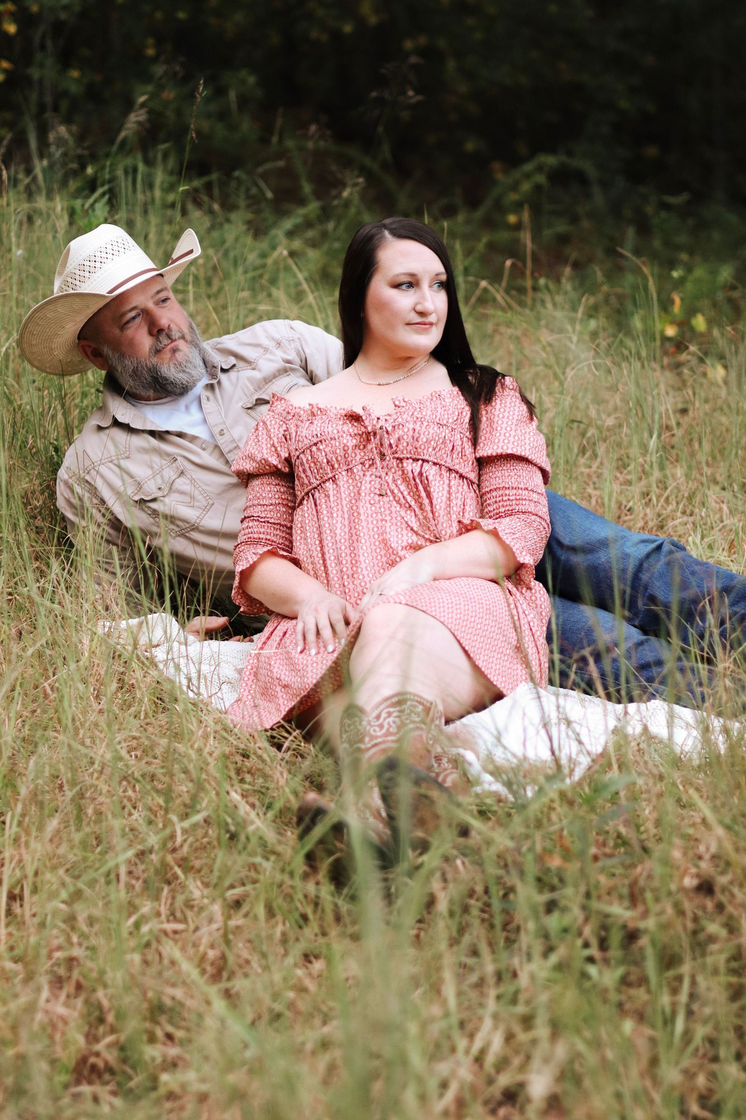 A couple lounges in tall grass during an outdoor photo session.