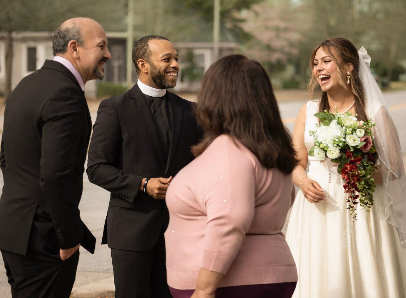 Wedding party members in formal attire stand together in a line outdoors.