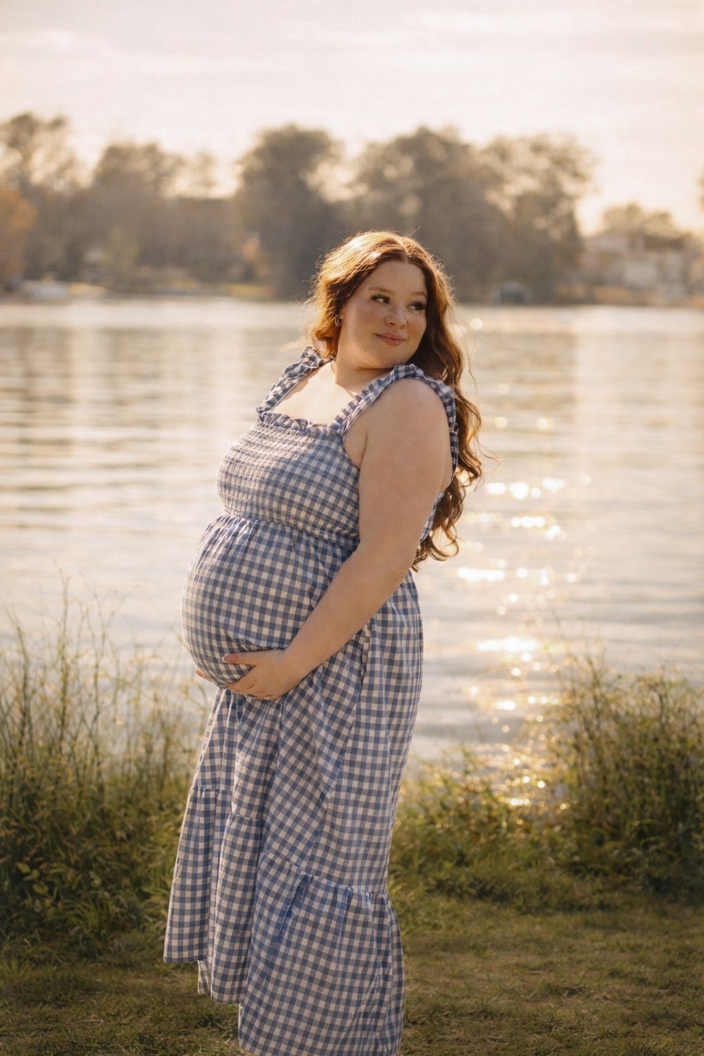A gingham dress-wearing figure stands by a sunlit lake at golden hour, creating a dreamy summer scene.