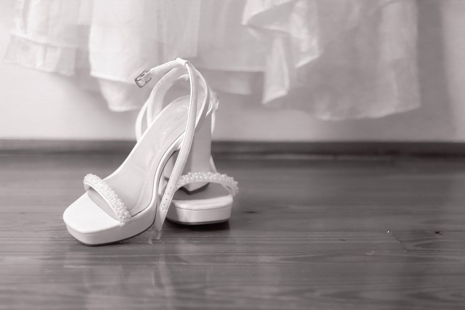 Black and white detail shots of a wedding dress and shoes on a wooden floor.