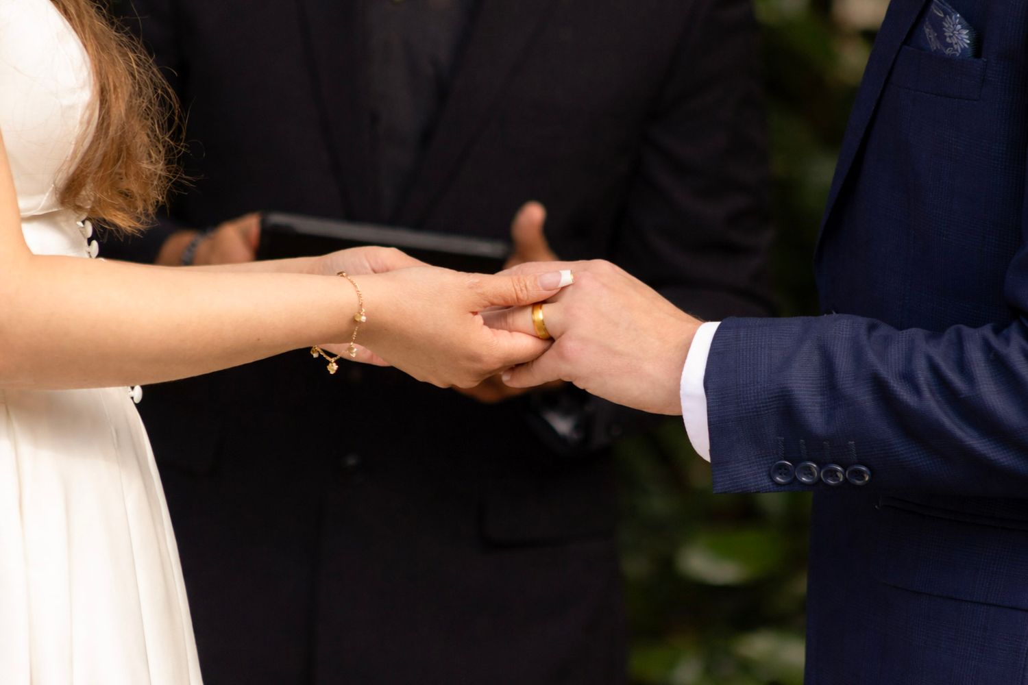 Close-up shot of hands exchanging wedding rings during an outdoor ceremony.