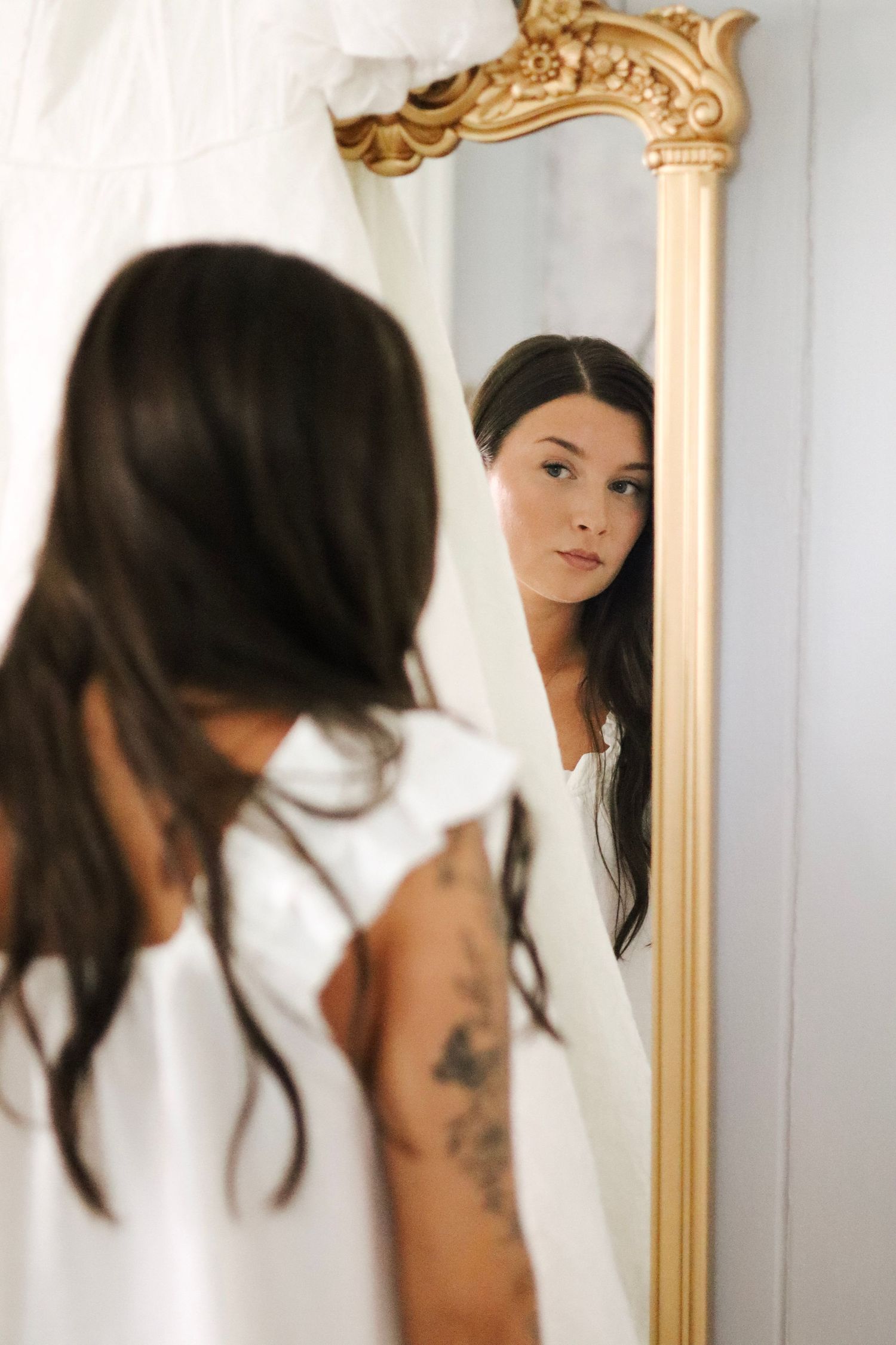 Artistic shots of a woman in white looking at her reflection in an ornate gold-framed mirror.