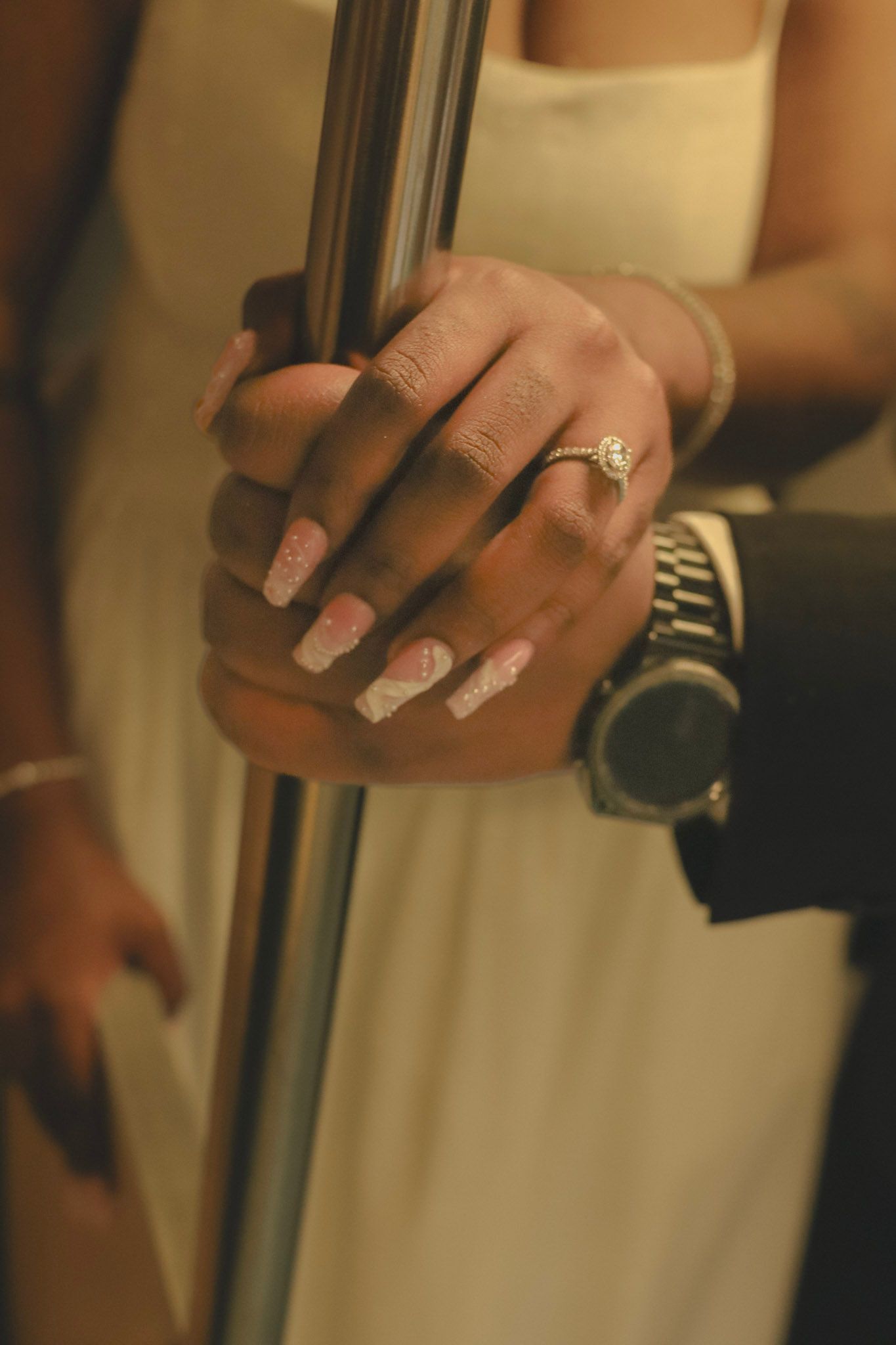 Close-up of bride and groom hands holding a pole, featuring a diamond engagement ring and luxury watch.