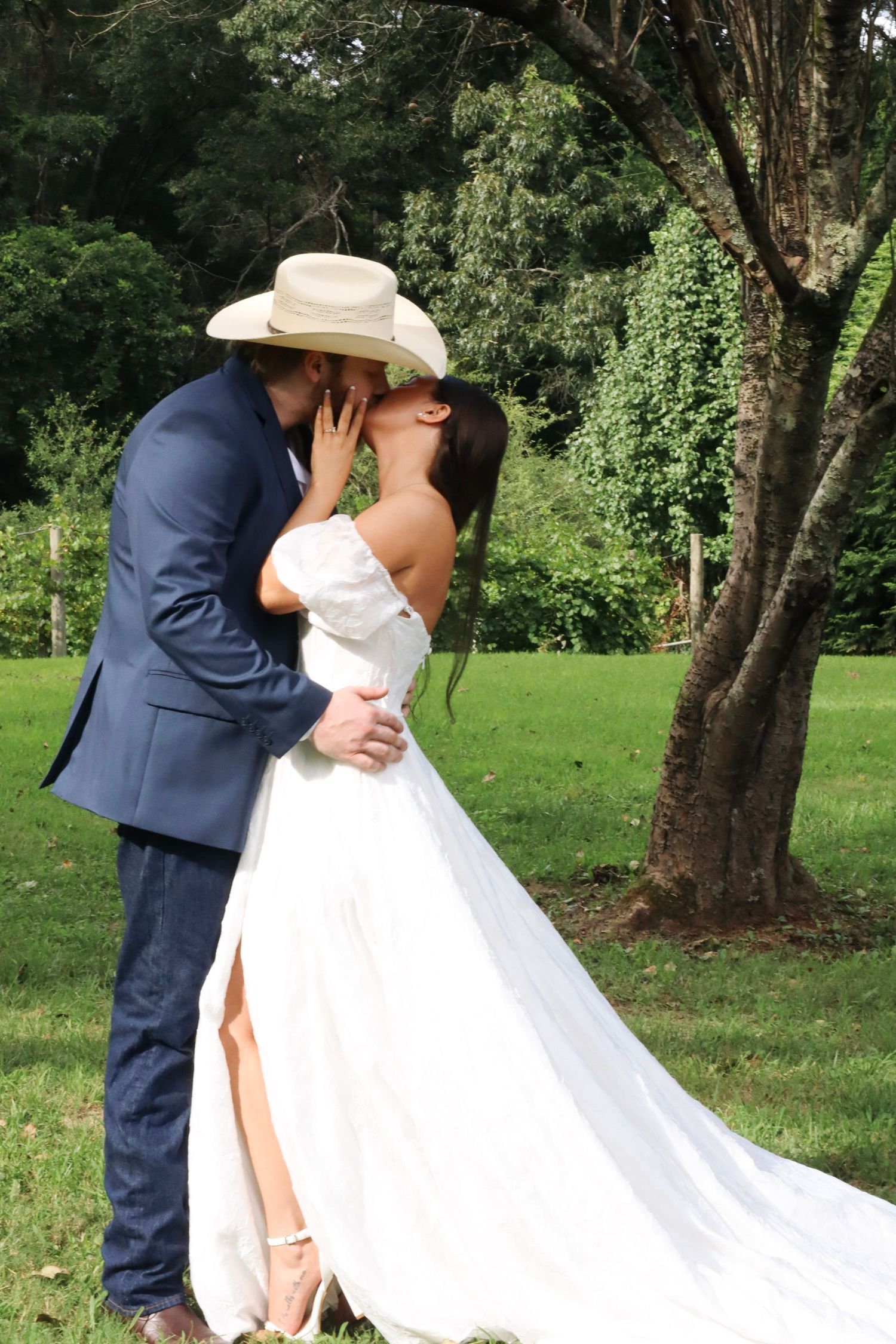 A couple shares an intimate moment in a garden setting wearing wedding attire with a flowing white dress and navy suit.