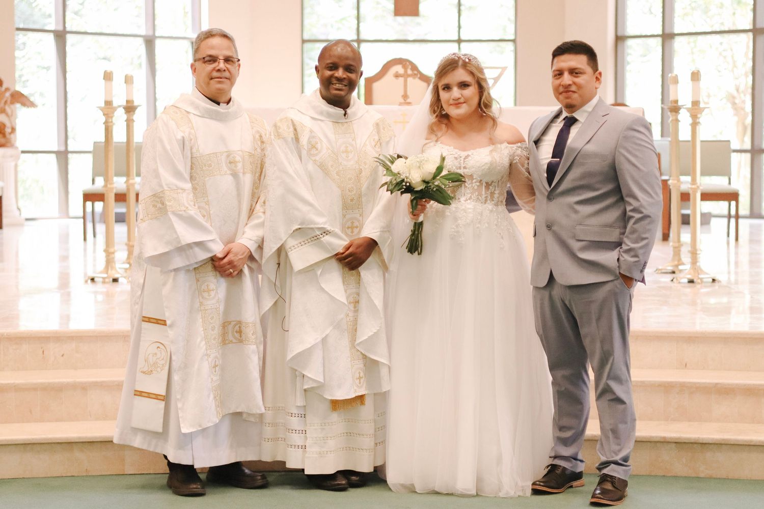 Wedding ceremony participants in white robes and gray suits stand together in a bright indoor space.