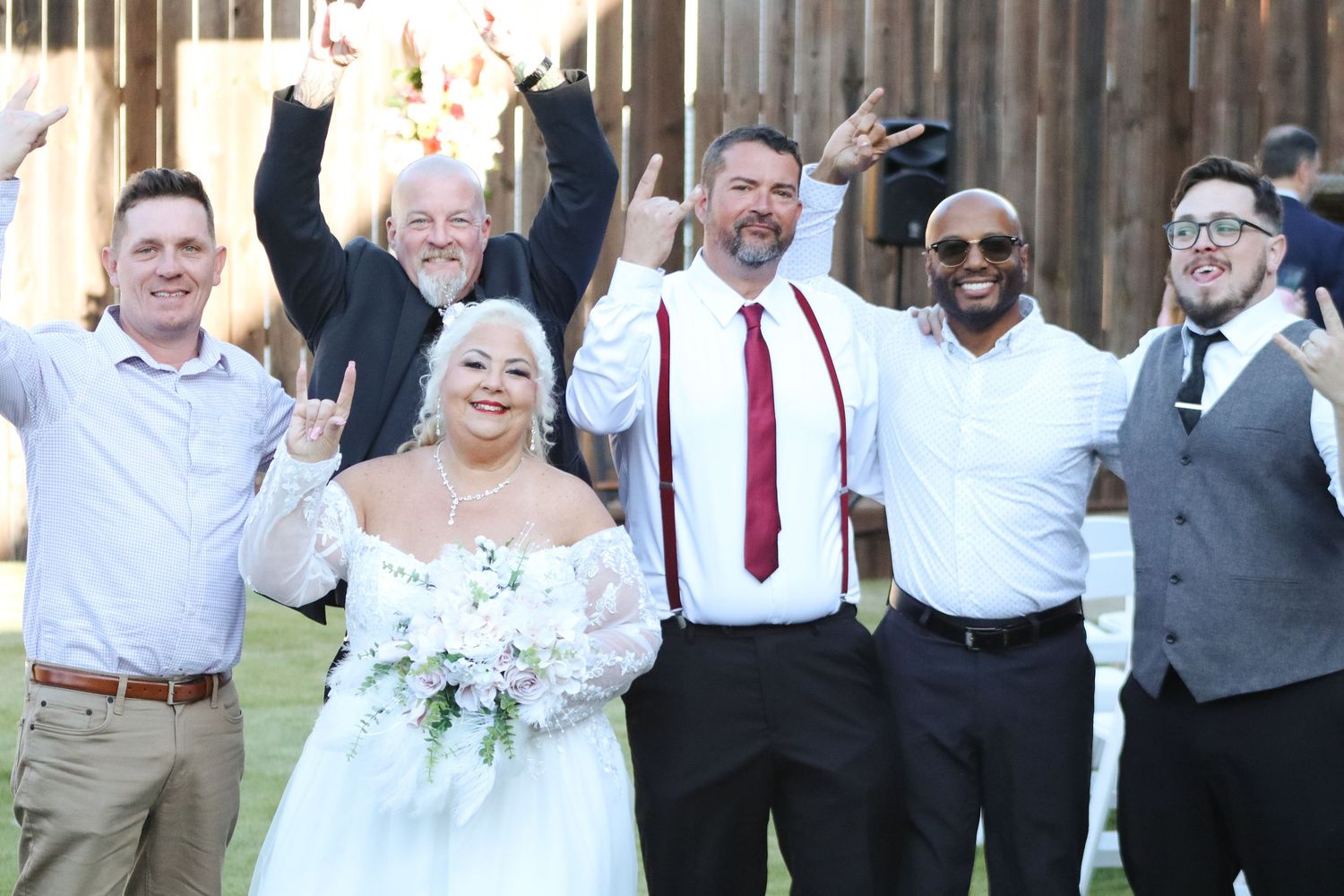 Wedding party in formal attire cheering and celebrating with arms raised outdoors.