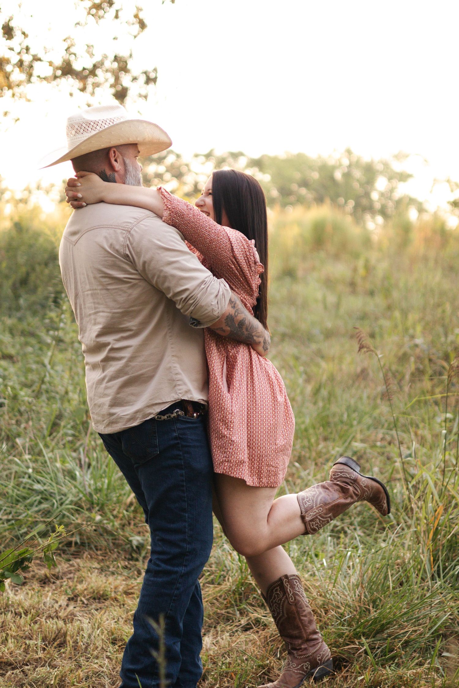 Couple in western attire embracing in golden sunset field.