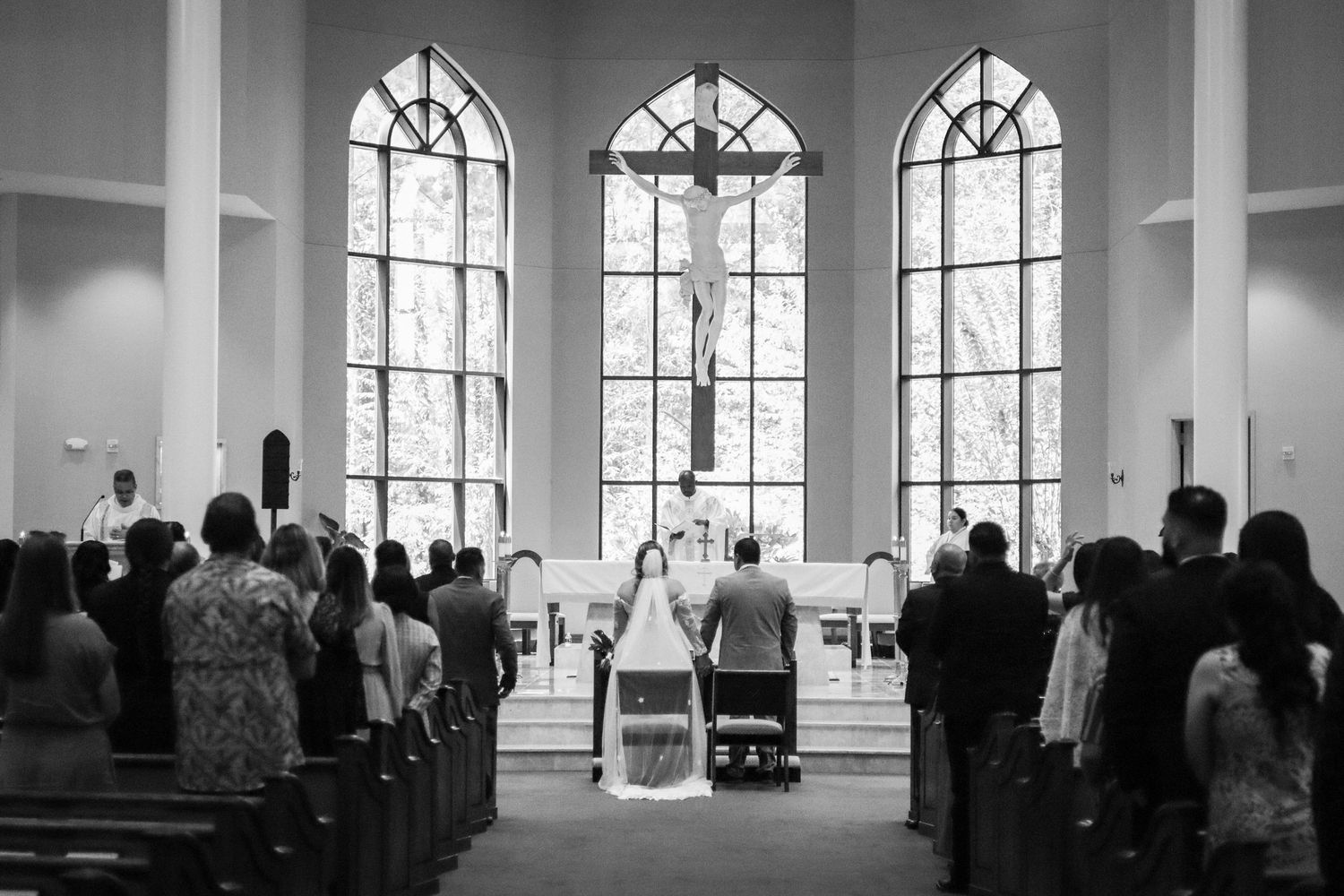 Church interior with arched windows silhouetted during wedding ceremony.
