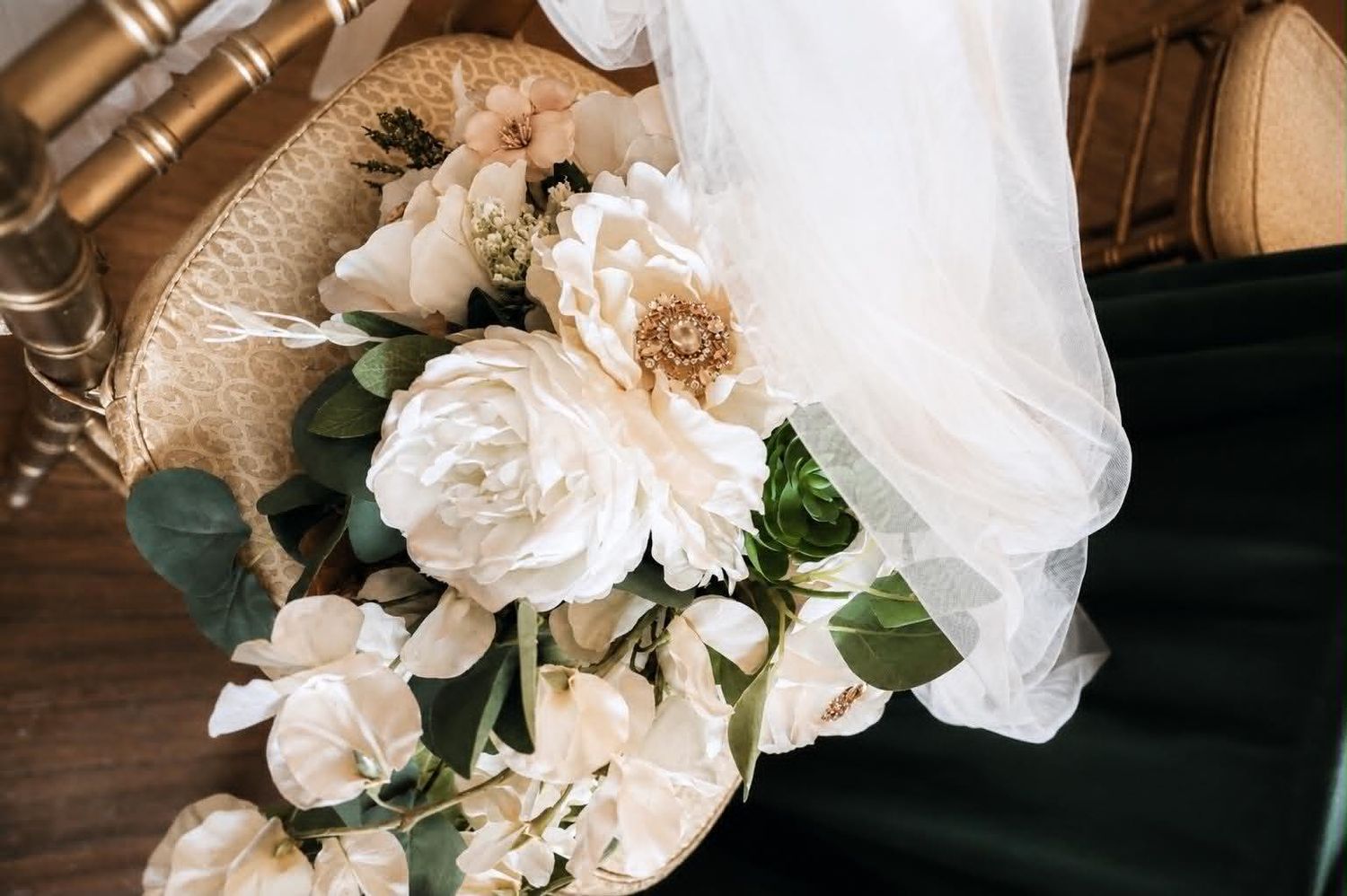 Elegant bridal bouquet of white peonies and roses with eucalyptus on a rattan chair with flowing veil.