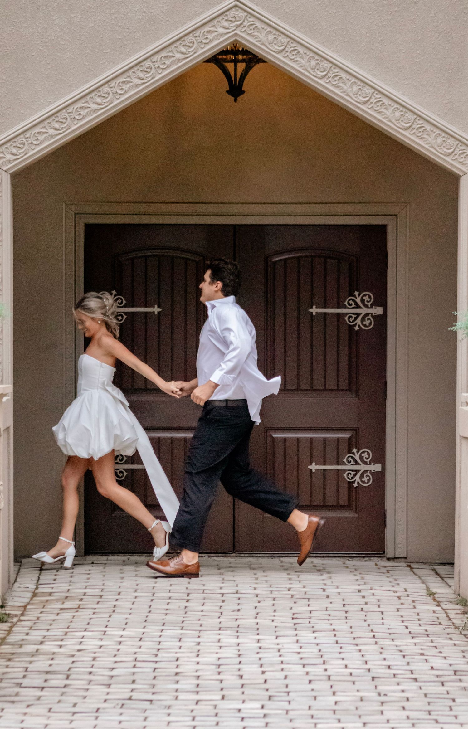 A playful wedding photo of a couple running through an arched doorway.