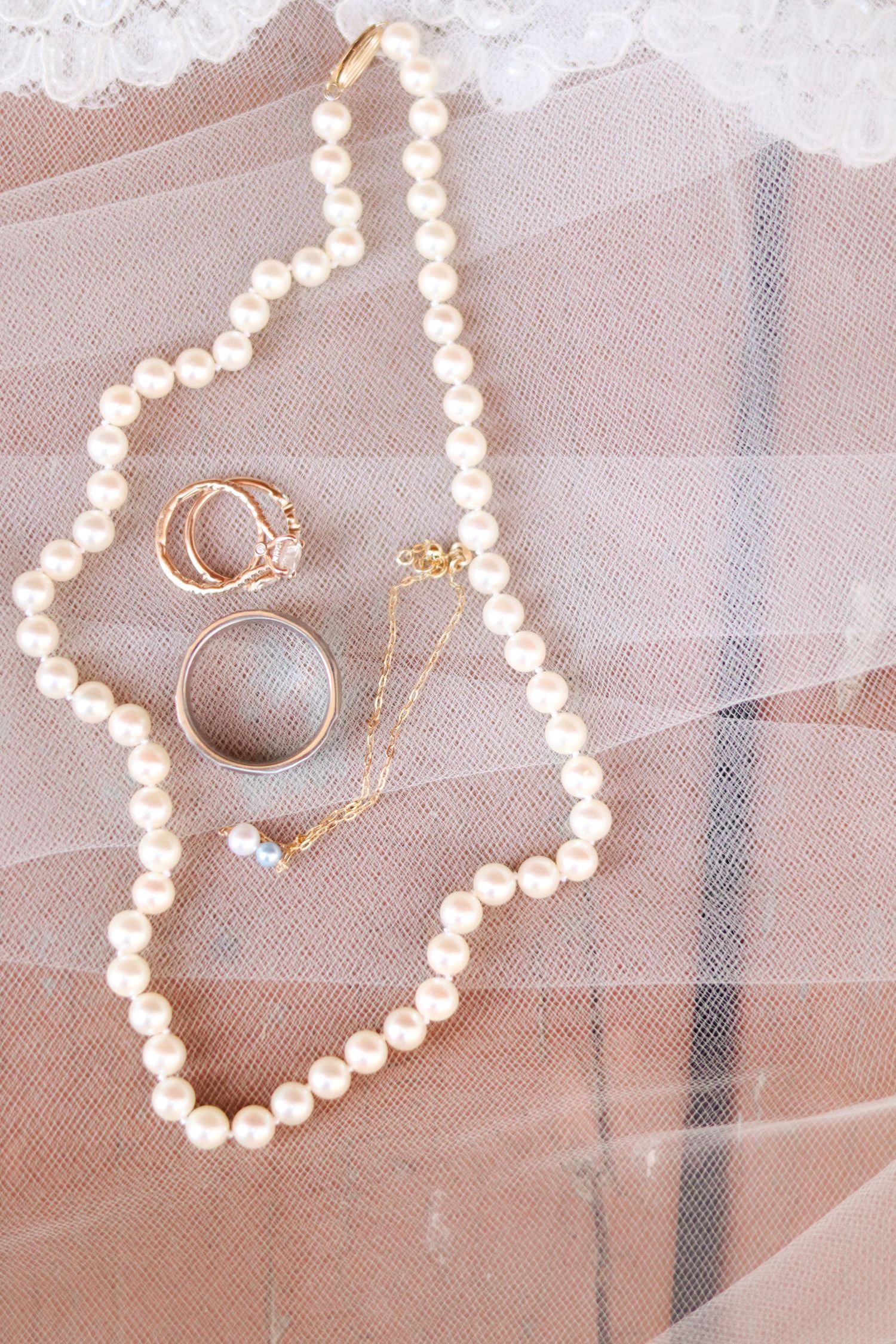 Pearl necklace and wedding rings arranged on delicate white tulle veil.