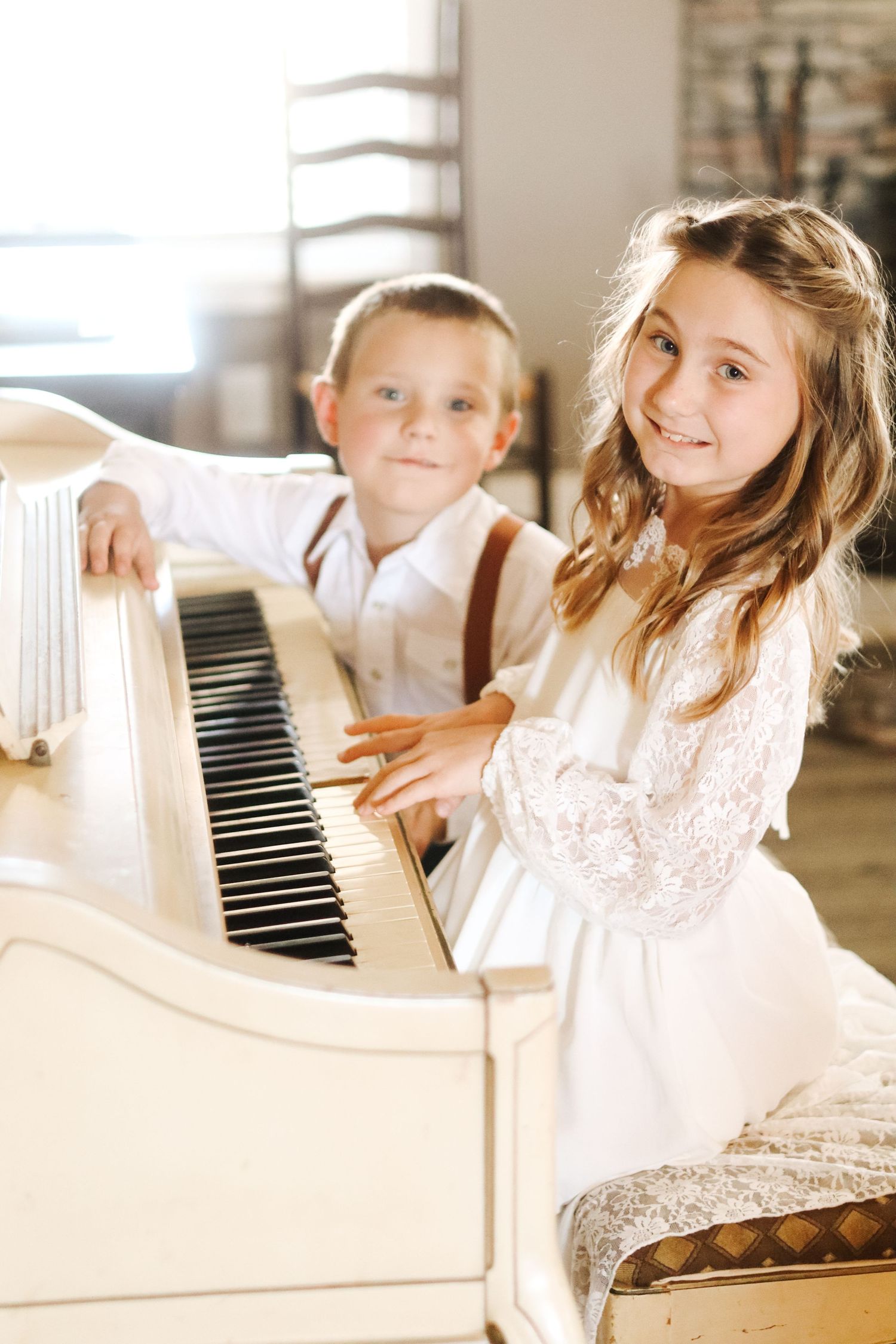 Children in white dresses play at an antique white piano.