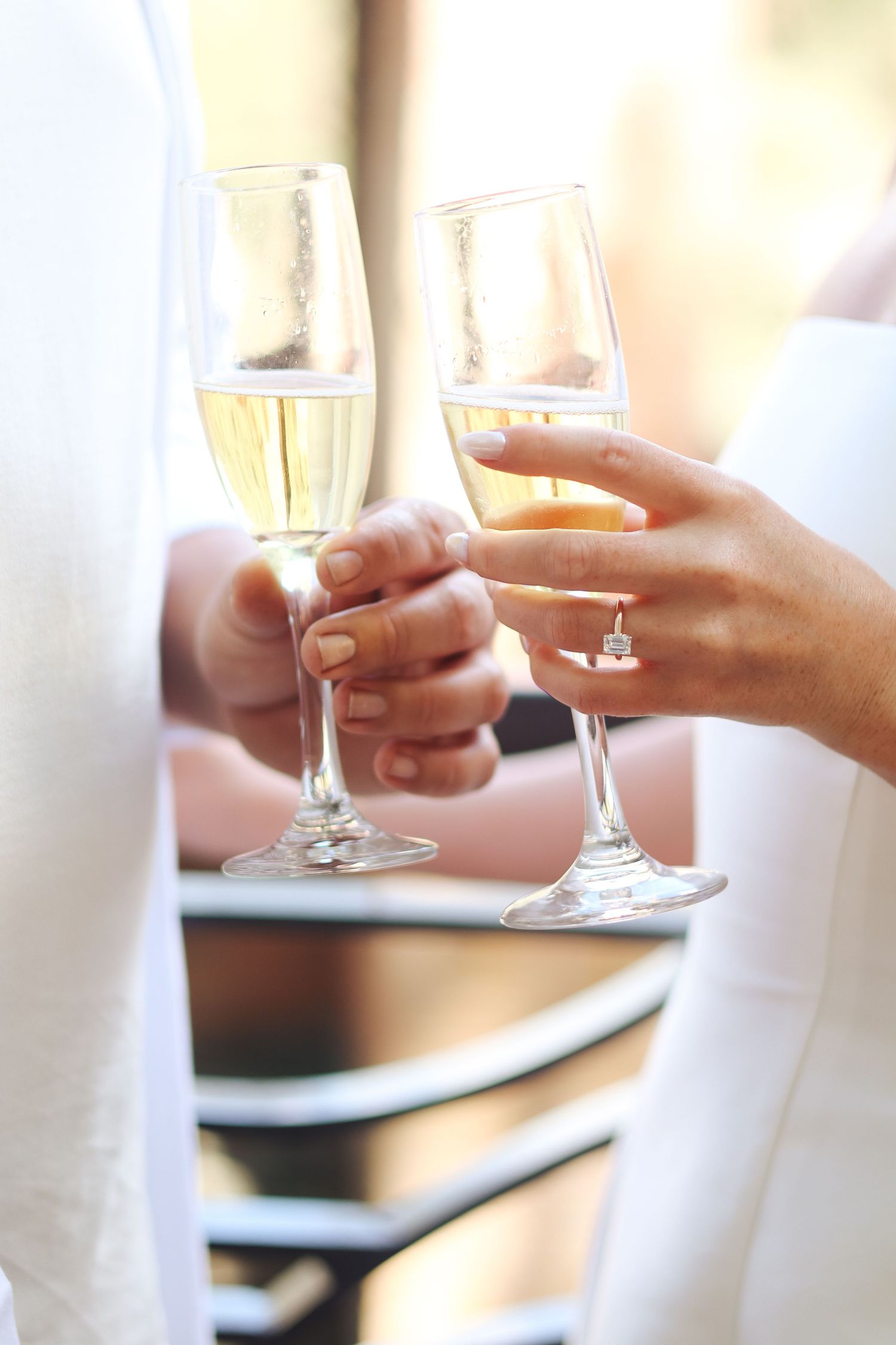 Hands holding champagne glasses for a wedding toast against a light background.
