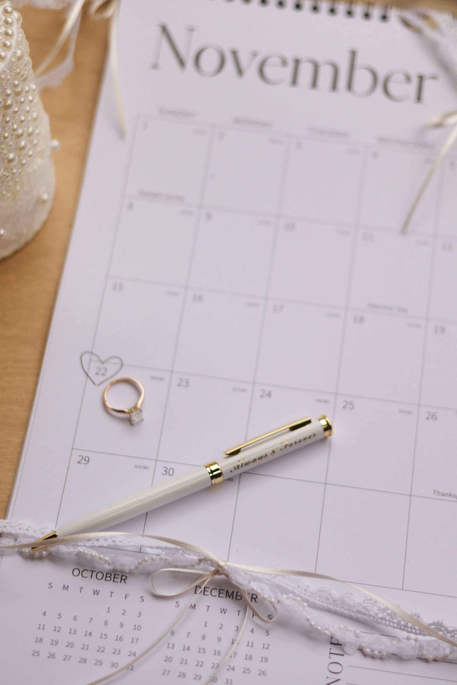 November calendar page with wedding rings and white pen on wooden surface.