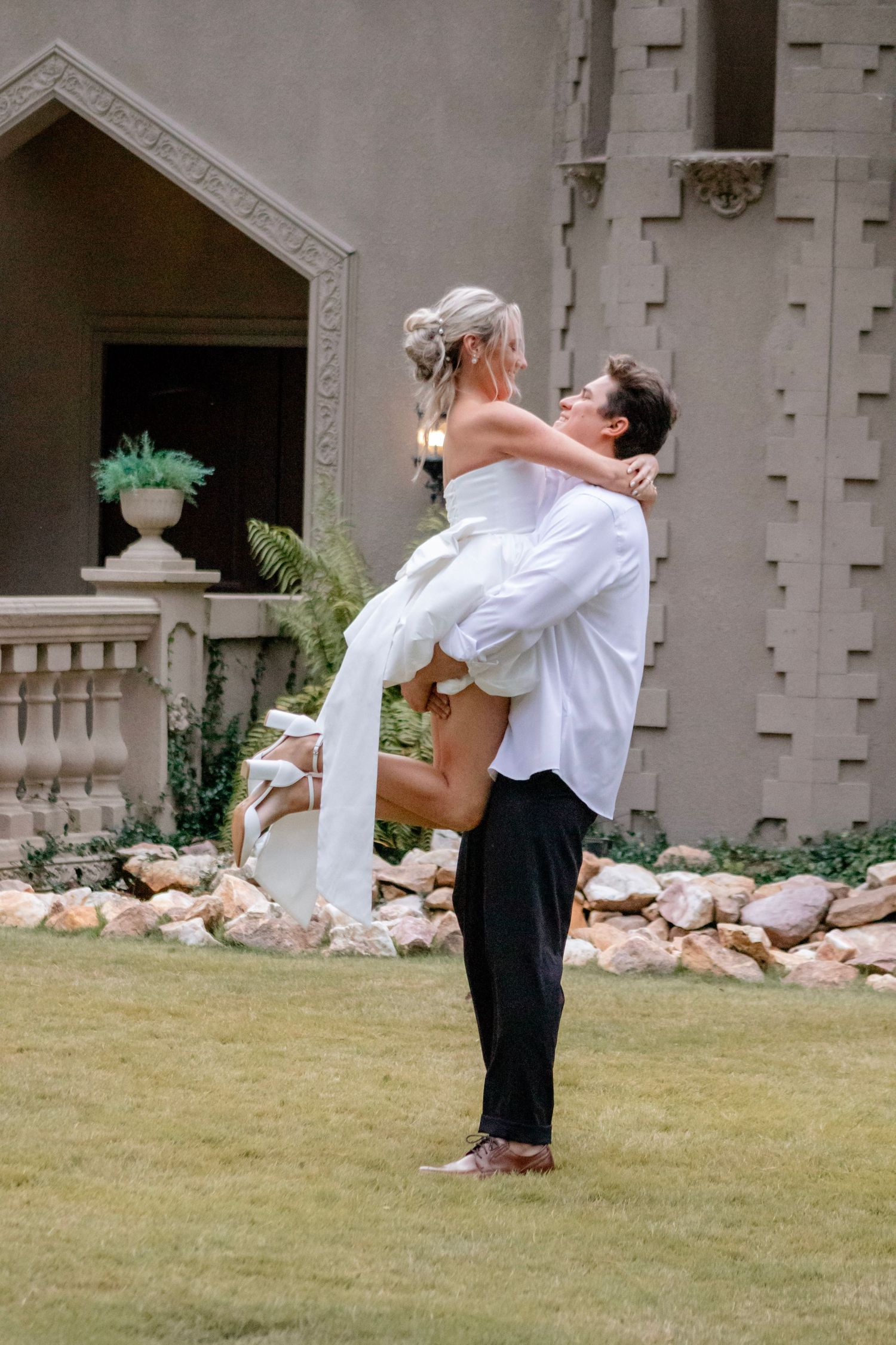 A joyful wedding moment captured on a lawn with architectural details in the background.