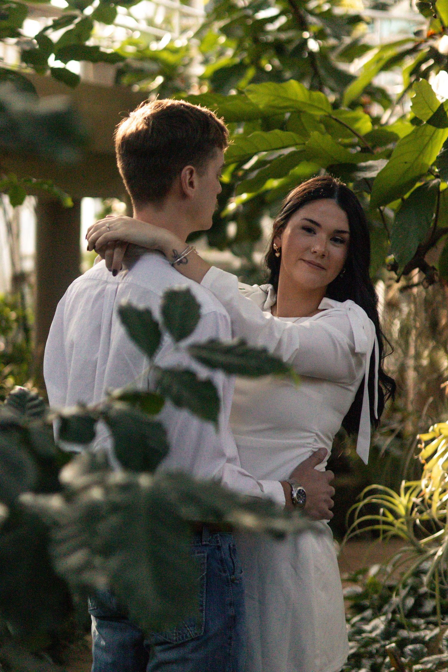 A couple shares an intimate moment together in a garden setting with green foliage in the background.