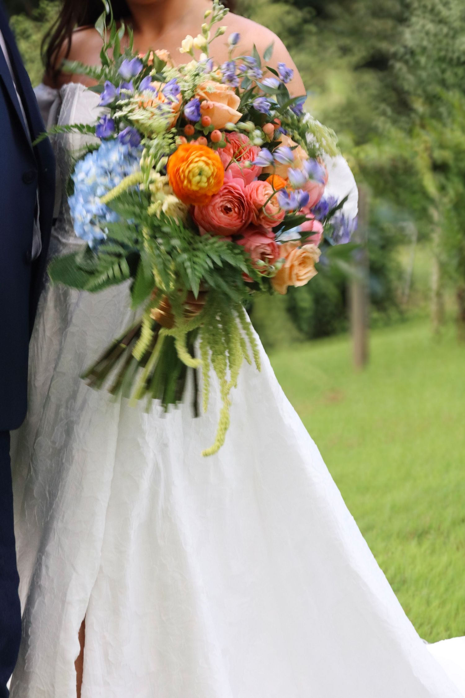 Close-up of vibrant orange and blue wedding bouquet against white wedding dress.