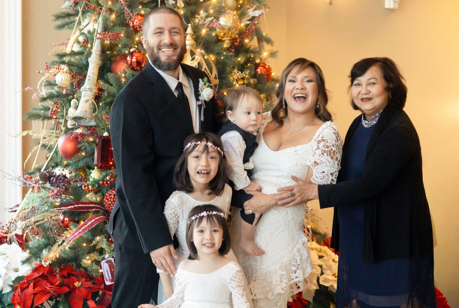 A family poses together for holiday photos in front of a decorated Christmas tree with twinkling lights.