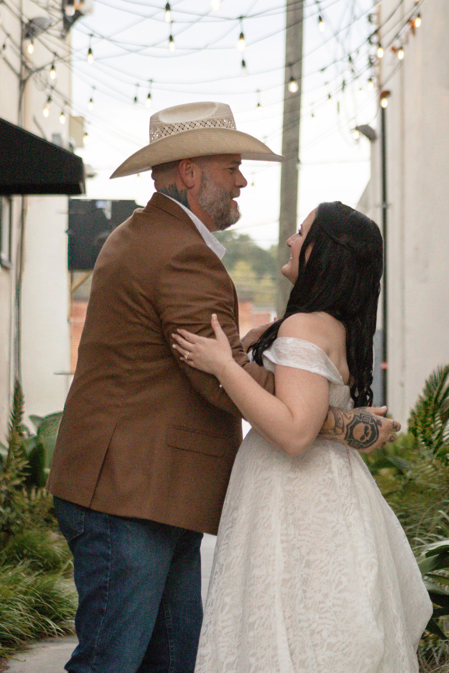 A romantic moment between a couple at an outdoor wedding venue with string lights overhead.