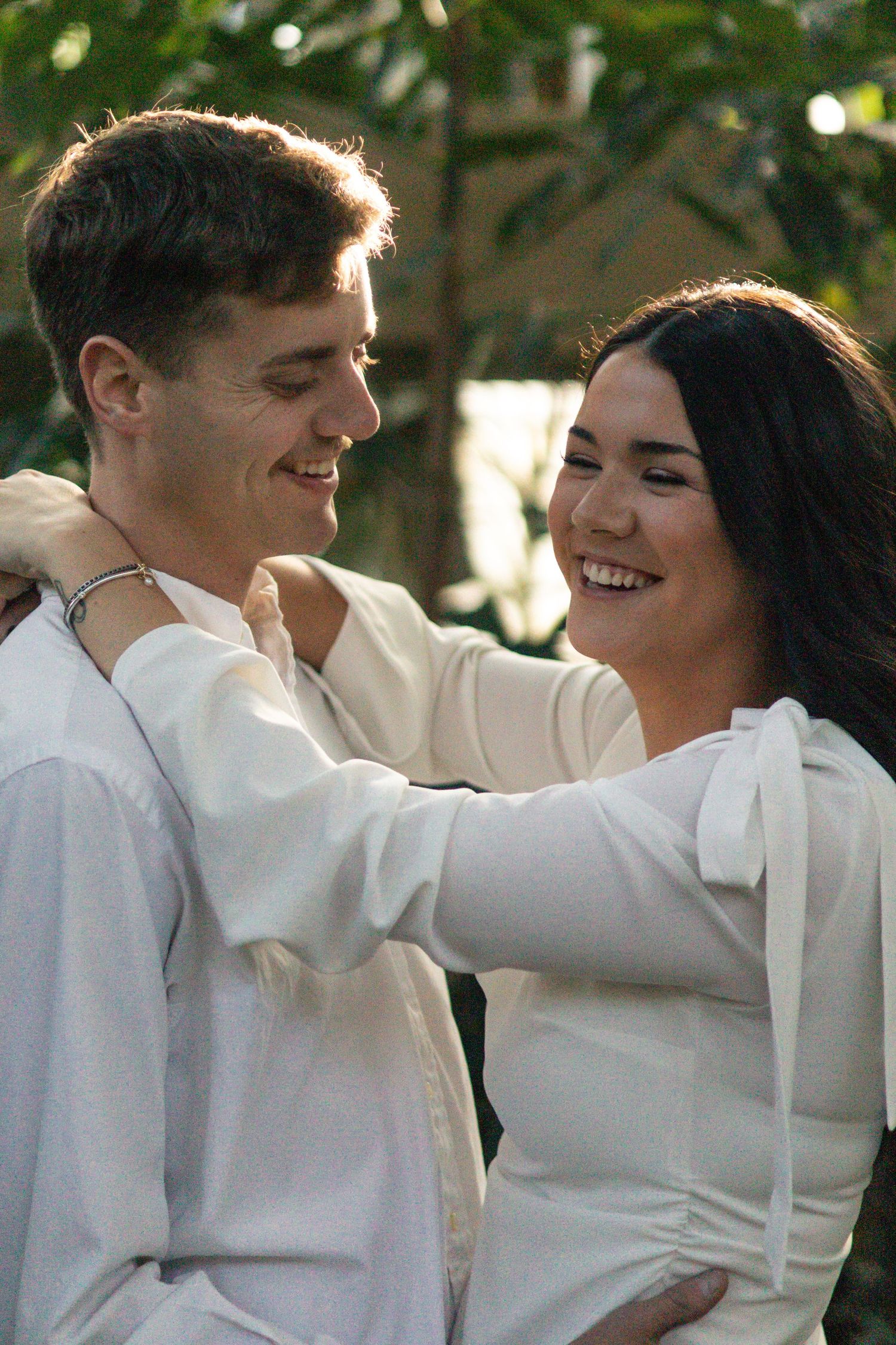 A couple in white formal attire share a romantic dance moment outdoors in natural lighting.