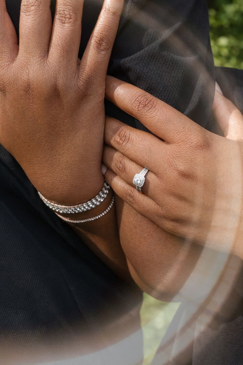 Close-up view of hands wearing elegant diamond rings and tennis bracelets against a dark background.