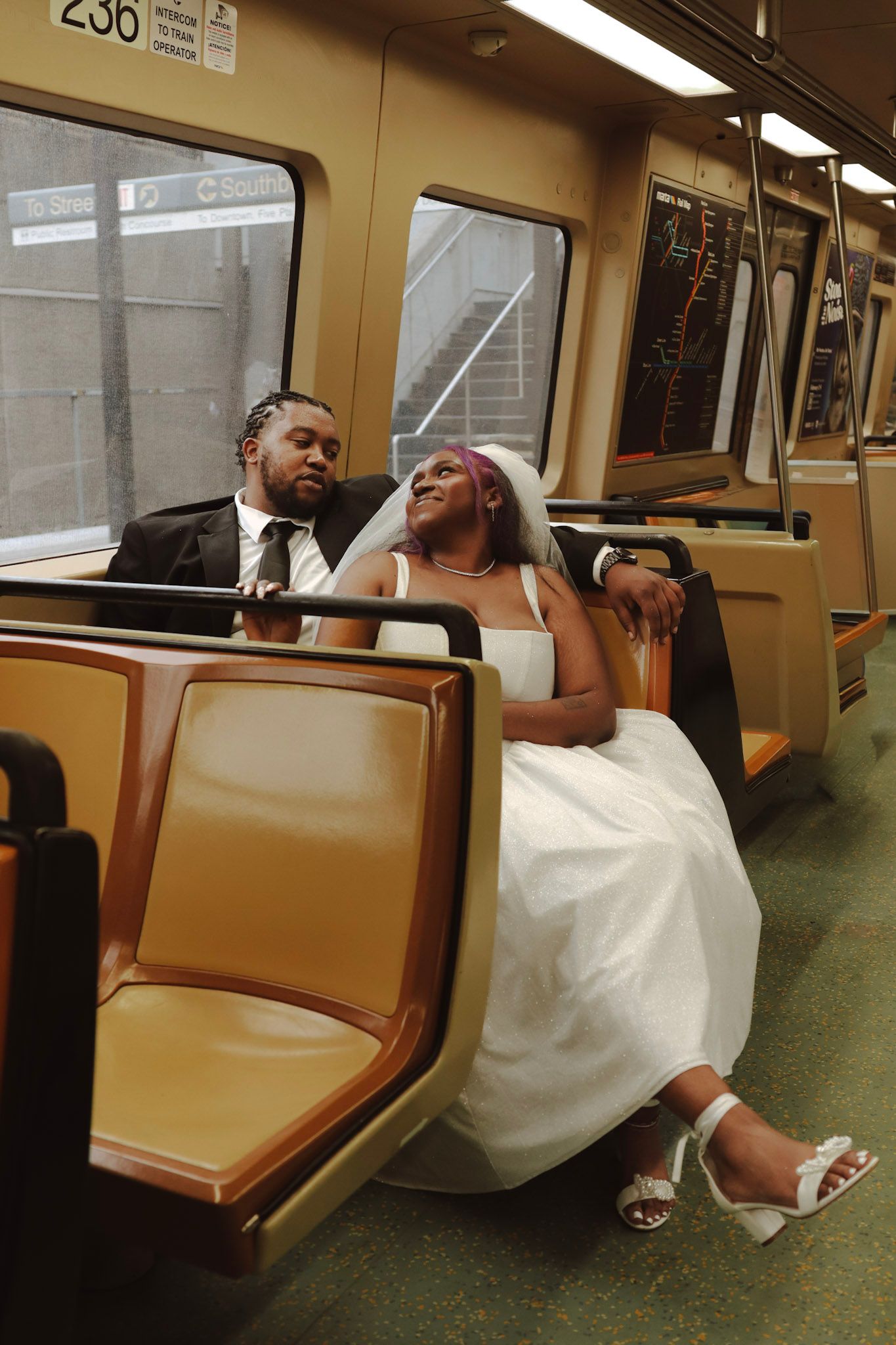Newlywed couple relaxing on a subway train, bride in white wedding dress and veil, groom in dark suit.