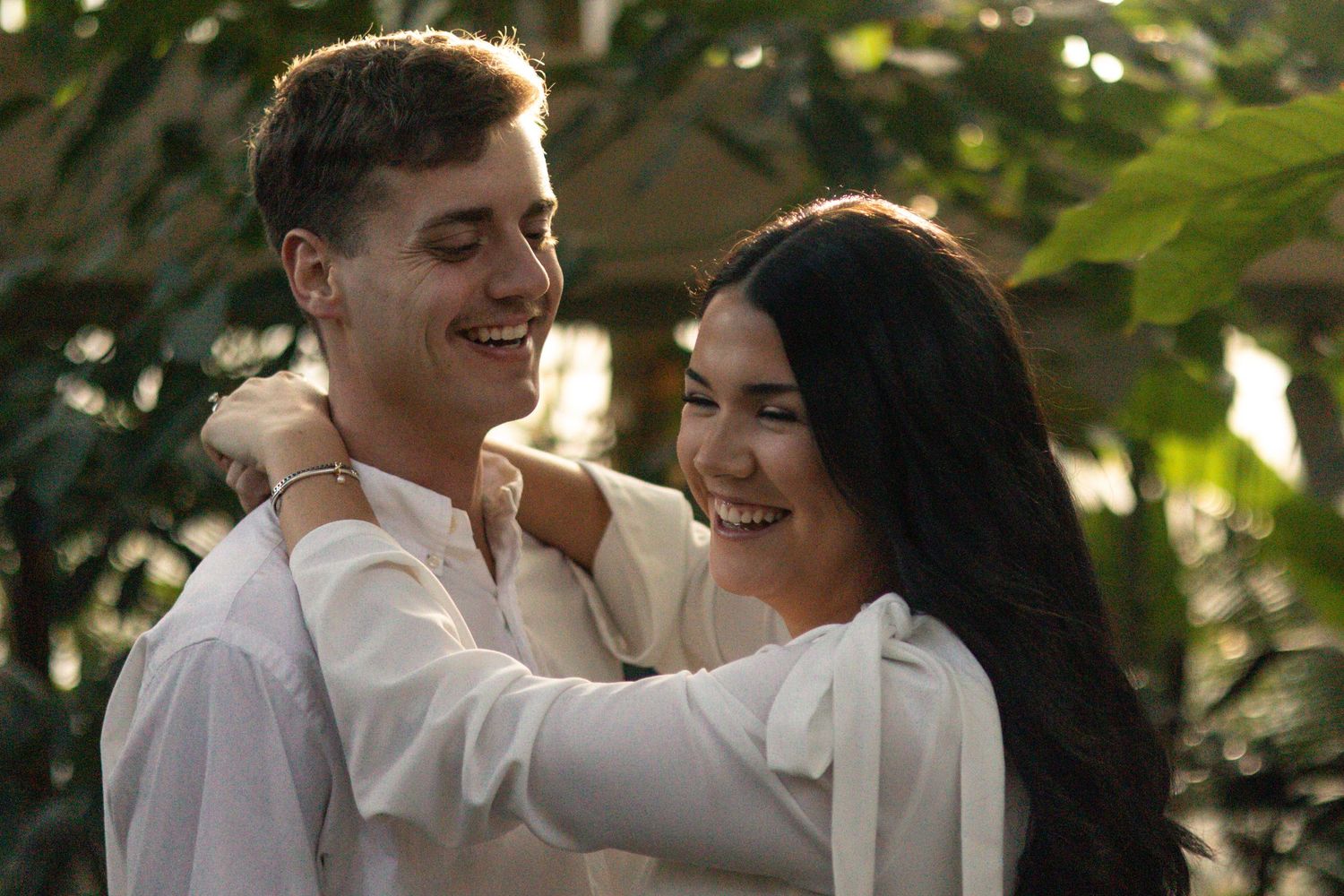 A couple shares intimate moments in a garden setting with natural sunlight filtering through trees.